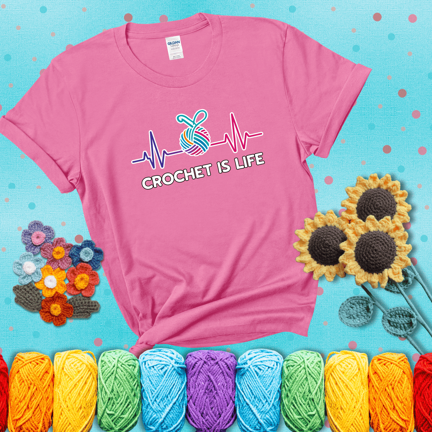 A heartbeat line with a colorful yarn ball and crochet hook in the center, with the words “Crochet is Life”, showing a pink tee with a teal sunflower background