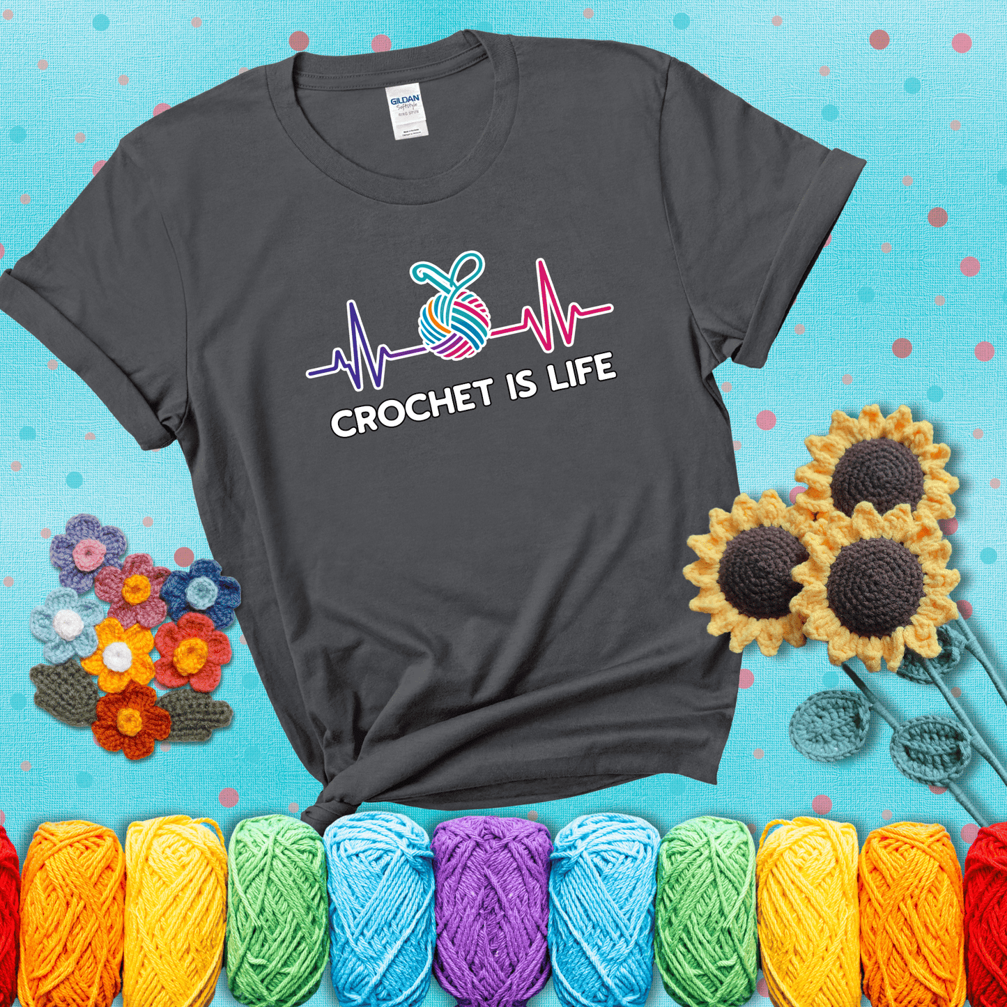 A heartbeat line with a colorful yarn ball and crochet hook in the center, with the words “Crochet is Life”, showing a dark grey tee with a teal sunflower background