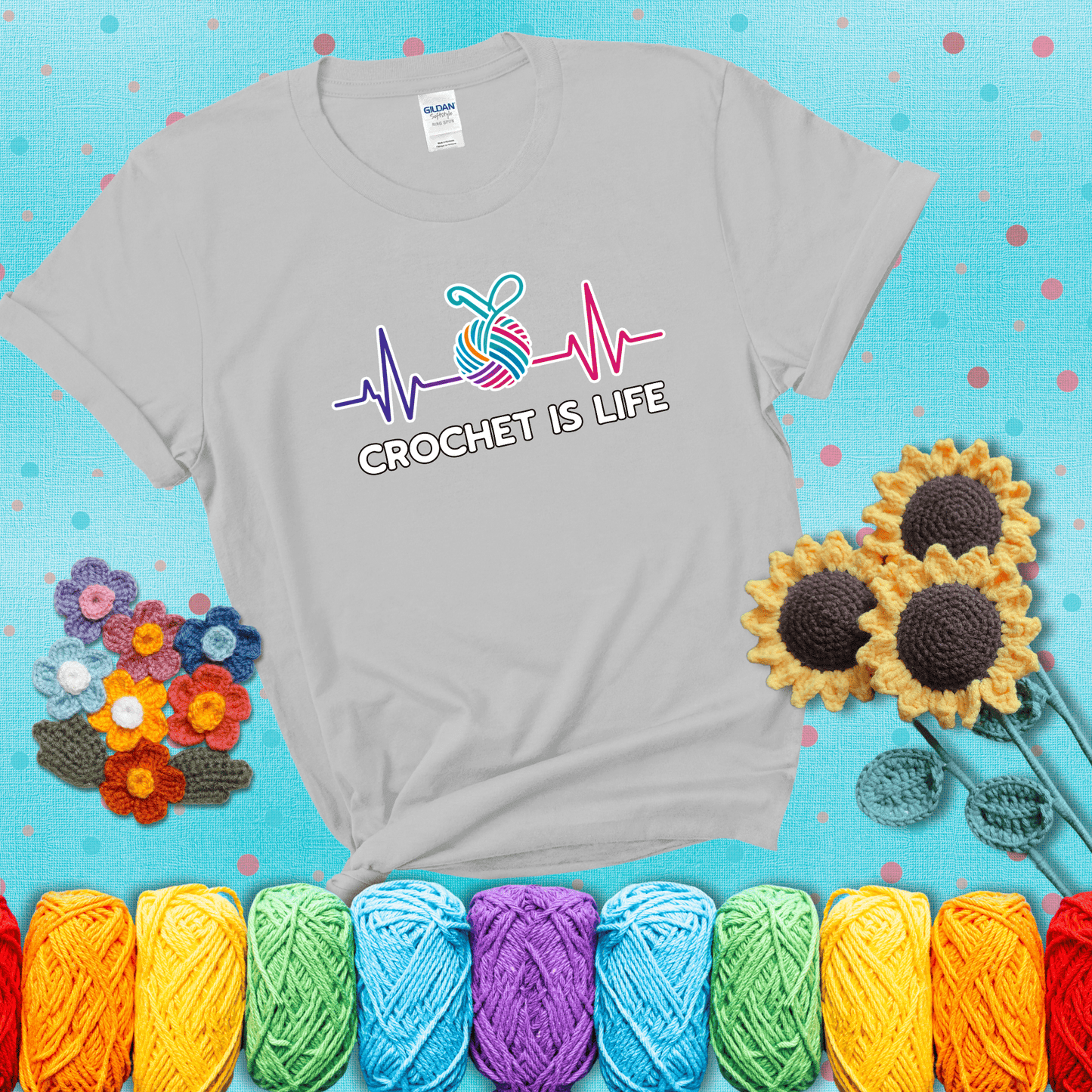 A heartbeat line with a colorful yarn ball and crochet hook in the center, with the words “Crochet is Life”, showing a light grey tee with a teal sunflower background