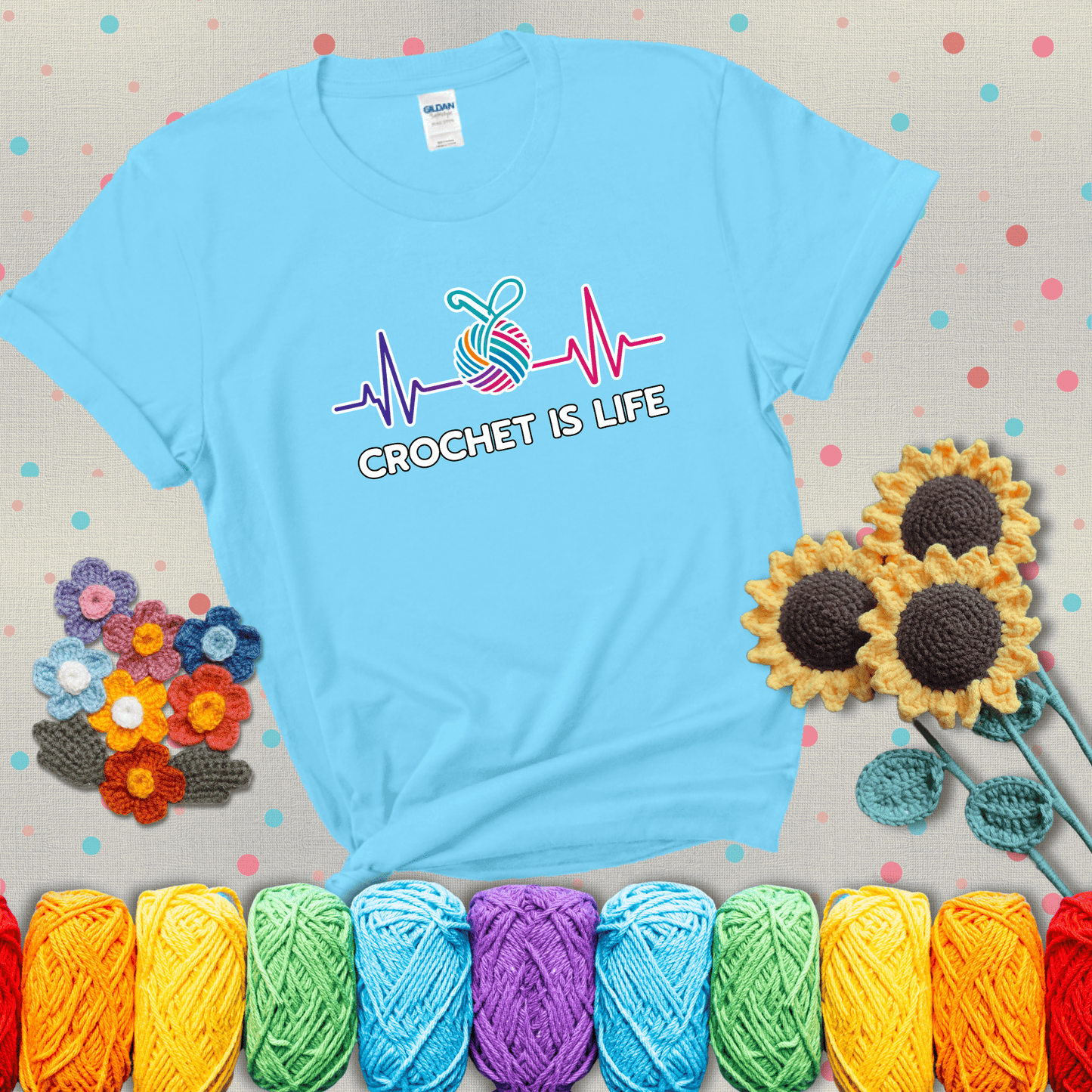 A heartbeat line with a colorful yarn ball and crochet hook in the center, with the words “Crochet is Life”, showing a light blue tee with grey sunflower background