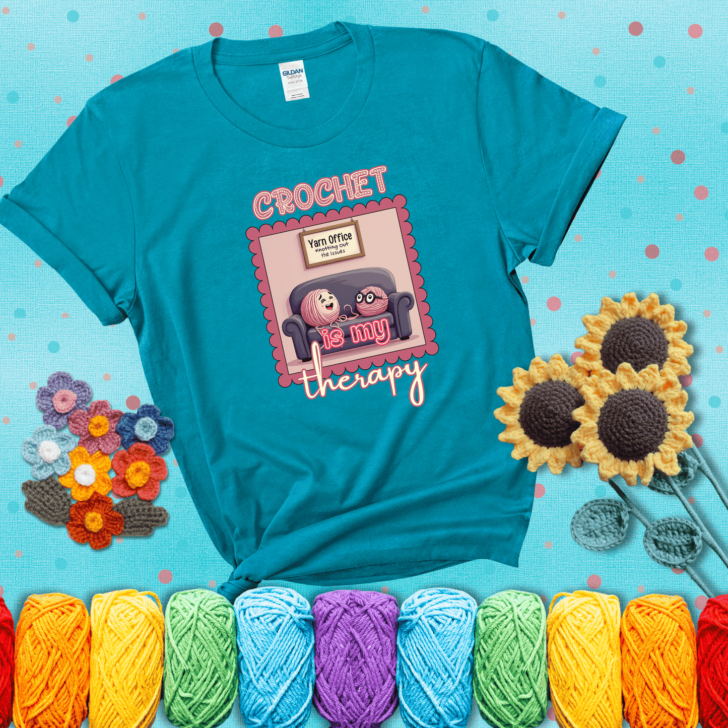 Simple text design with soothing yarn elements. Text reads: “Crochet is My Therapy.” A calming tee for fiber lovers who find healing in every stitch; showing a blue-green tee with a teal sunflower background