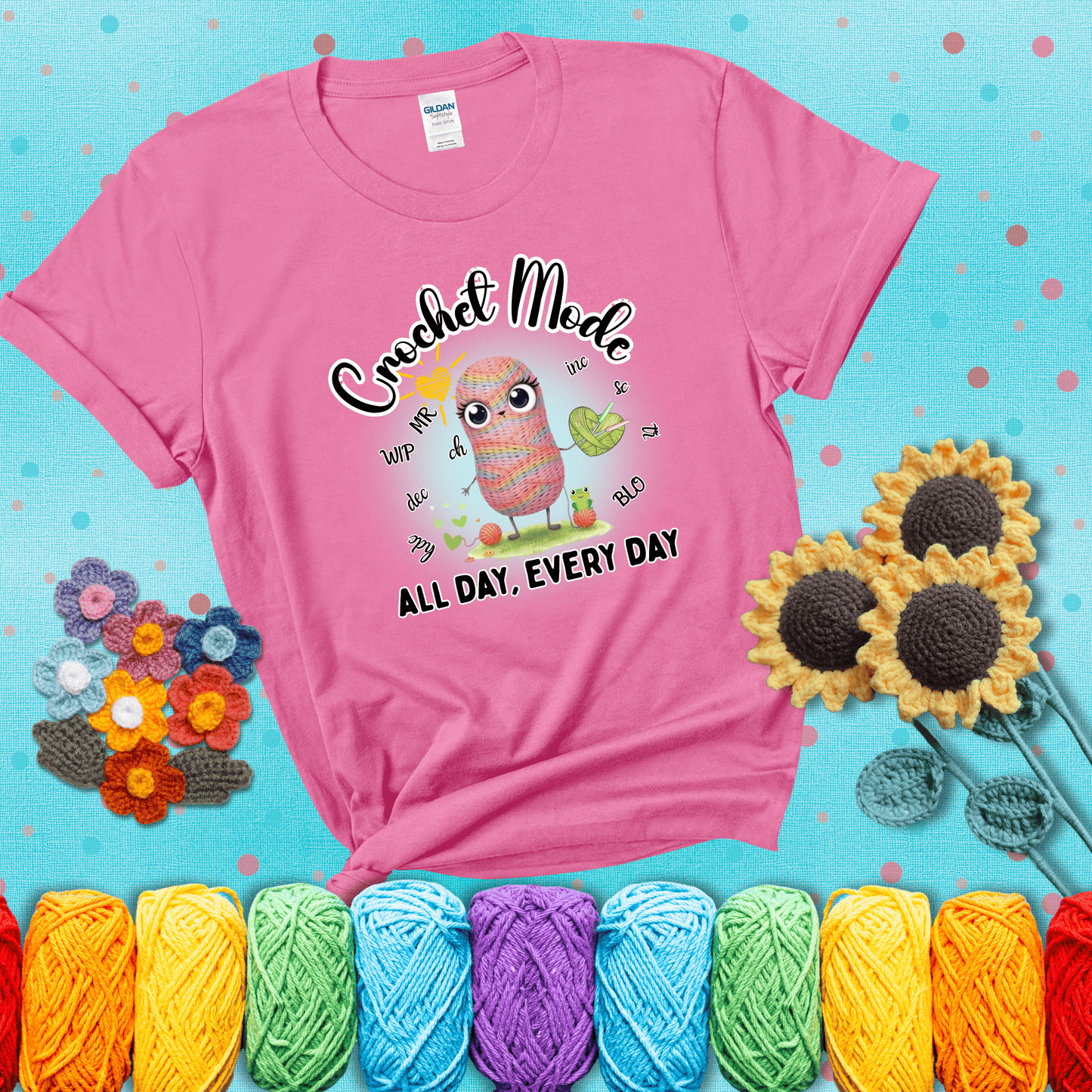 A kawaii-style rainbow yarn character surrounded by crochet stitch abbreviations and holding a yarn heart, with text “Crochet Mode All Day, Every Day"; showing a pink tee with a teal sunflower background
