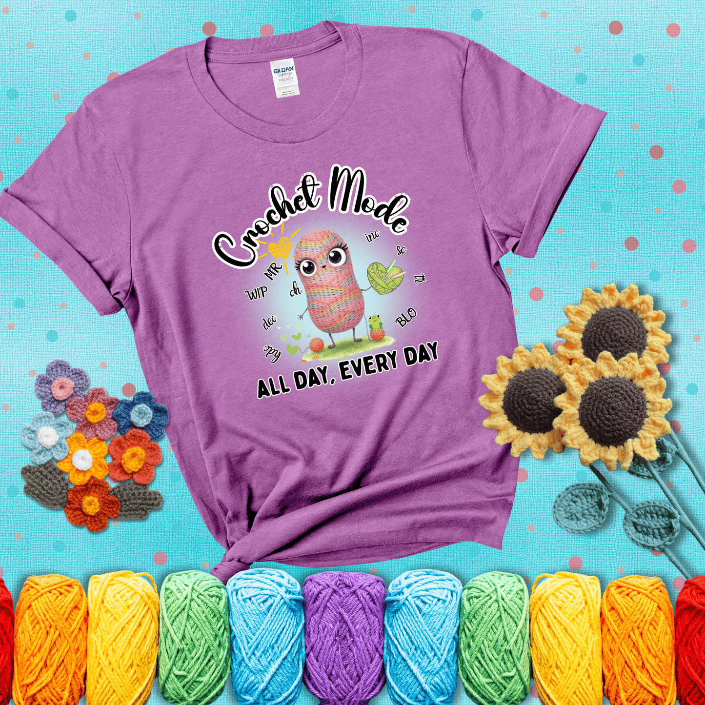 A kawaii-style rainbow yarn character surrounded by crochet stitch abbreviations and holding a yarn heart, with text “Crochet Mode All Day, Every Day"; showing a light purple tee with a teal sunflower background