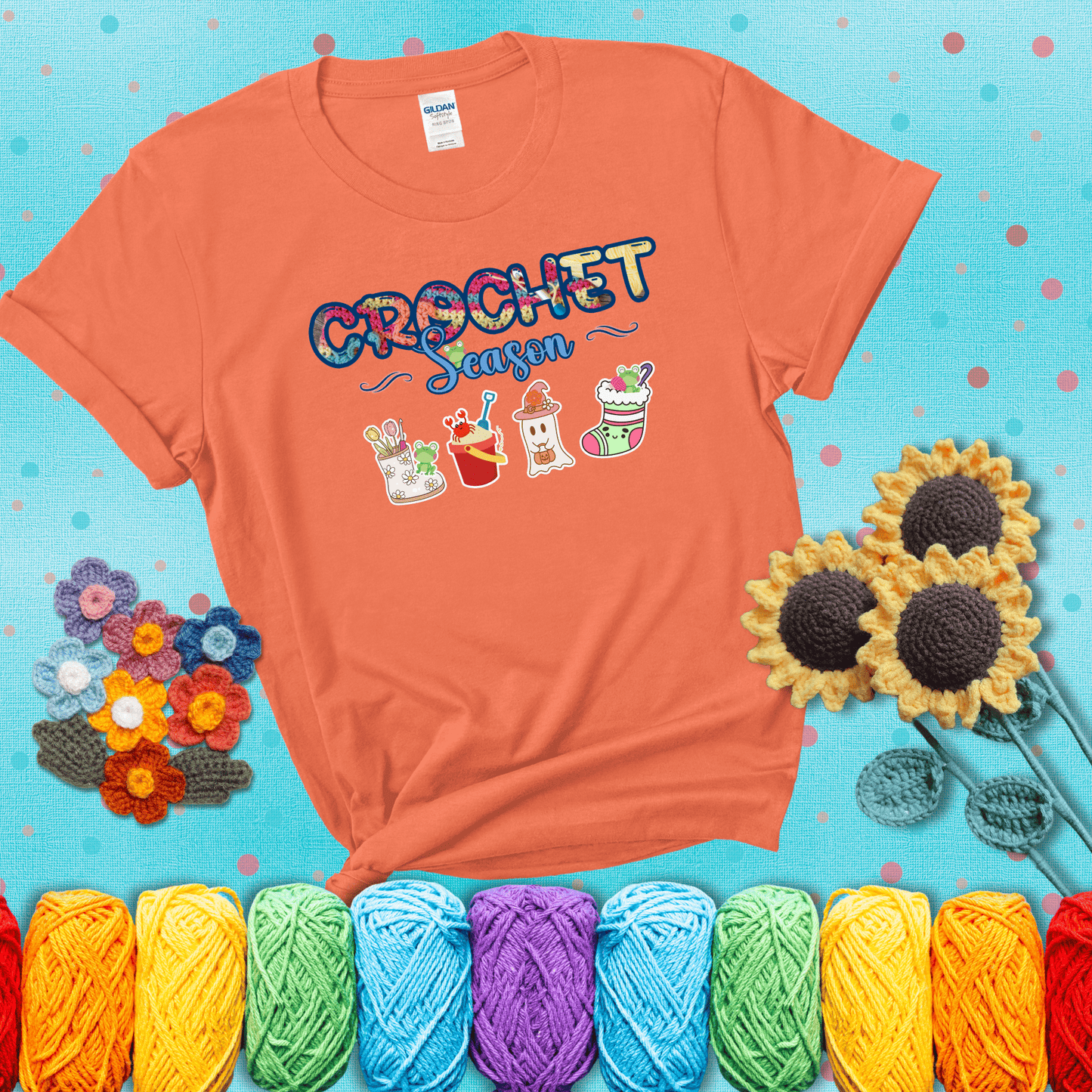 The words “Crochet Season” with cute seasonal icons below: a spring boot with hooks, summer bucket with crab, fall ghost with pumpkin hat, and winter stocking - all with tiny frogs; showing a light orange tee with a teal sunflower background