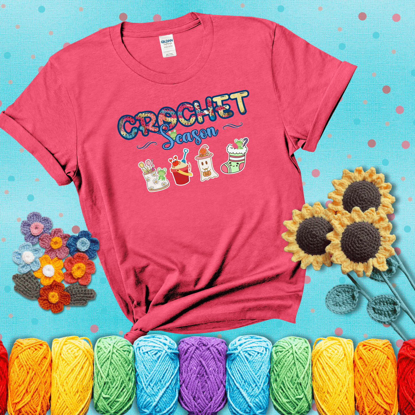 The words “Crochet Season” with cute seasonal icons below: a spring boot with hooks, summer bucket with crab, fall ghost with pumpkin hat, and winter stocking - all with tiny frogs; showing a light red tee with a teal sunflower background