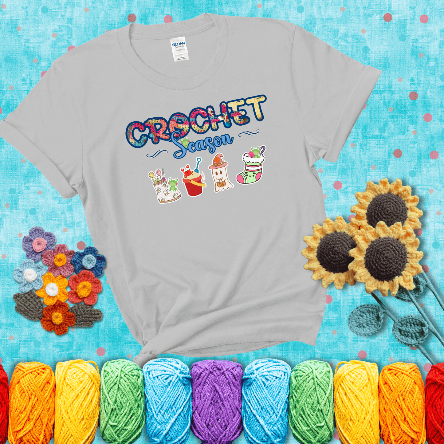 The words “Crochet Season” with cute seasonal icons below: a spring boot with hooks, summer bucket with crab, fall ghost with pumpkin hat, and winter stocking - all with tiny frogs; showing a light grey tee with a teal sunflower background