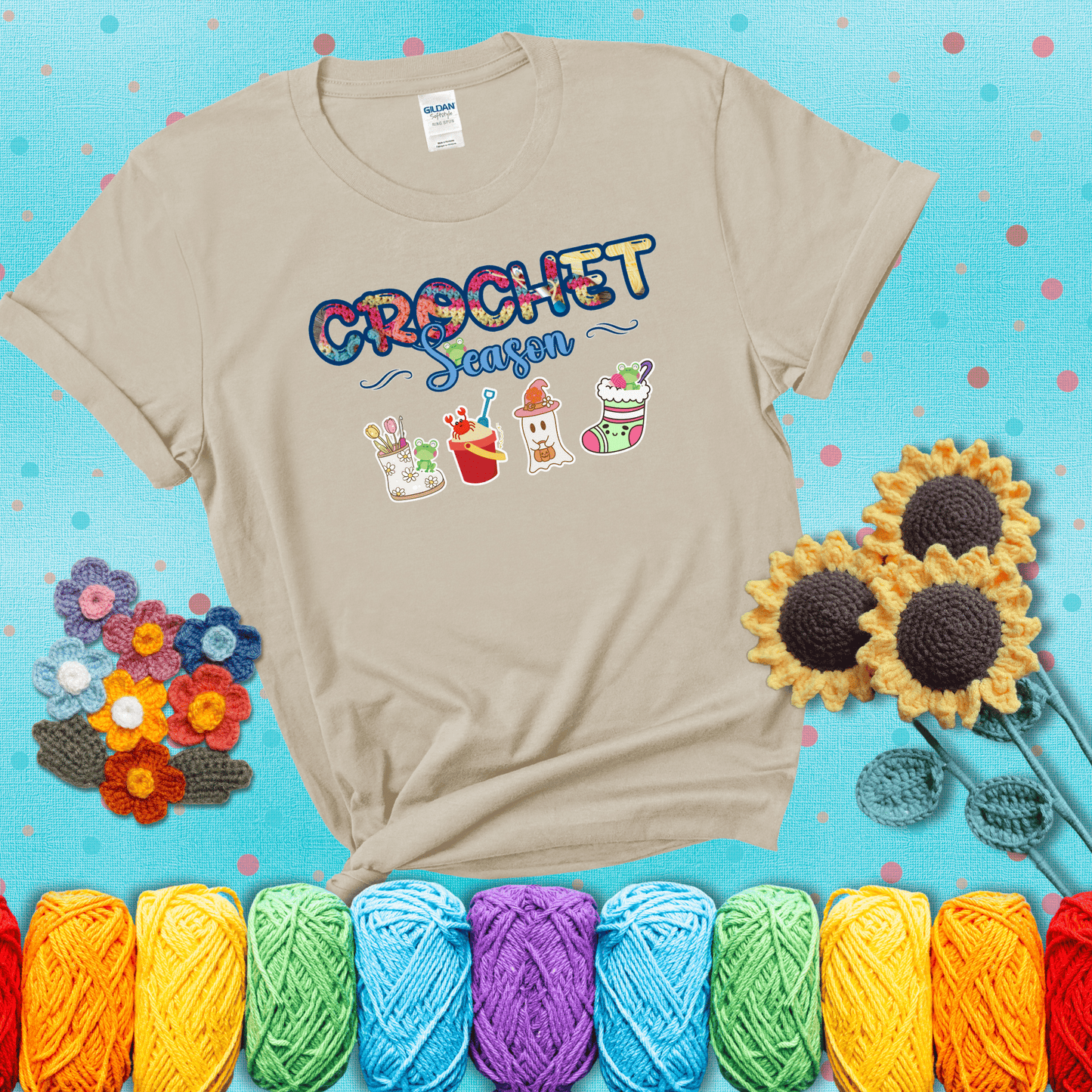 The words “Crochet Season” with cute seasonal icons below: a spring boot with hooks, summer bucket with crab, fall ghost with pumpkin hat, and winter stocking - all with tiny frogs; showing a beige tee with a teal sunflower background