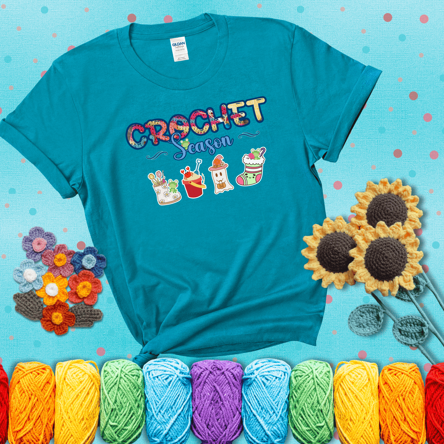 The words “Crochet Season” with cute seasonal icons below: a spring boot with hooks, summer bucket with crab, fall ghost with pumpkin hat, and winter stocking - all with tiny frogs; showing a blue-green tee with a teal sunflower background