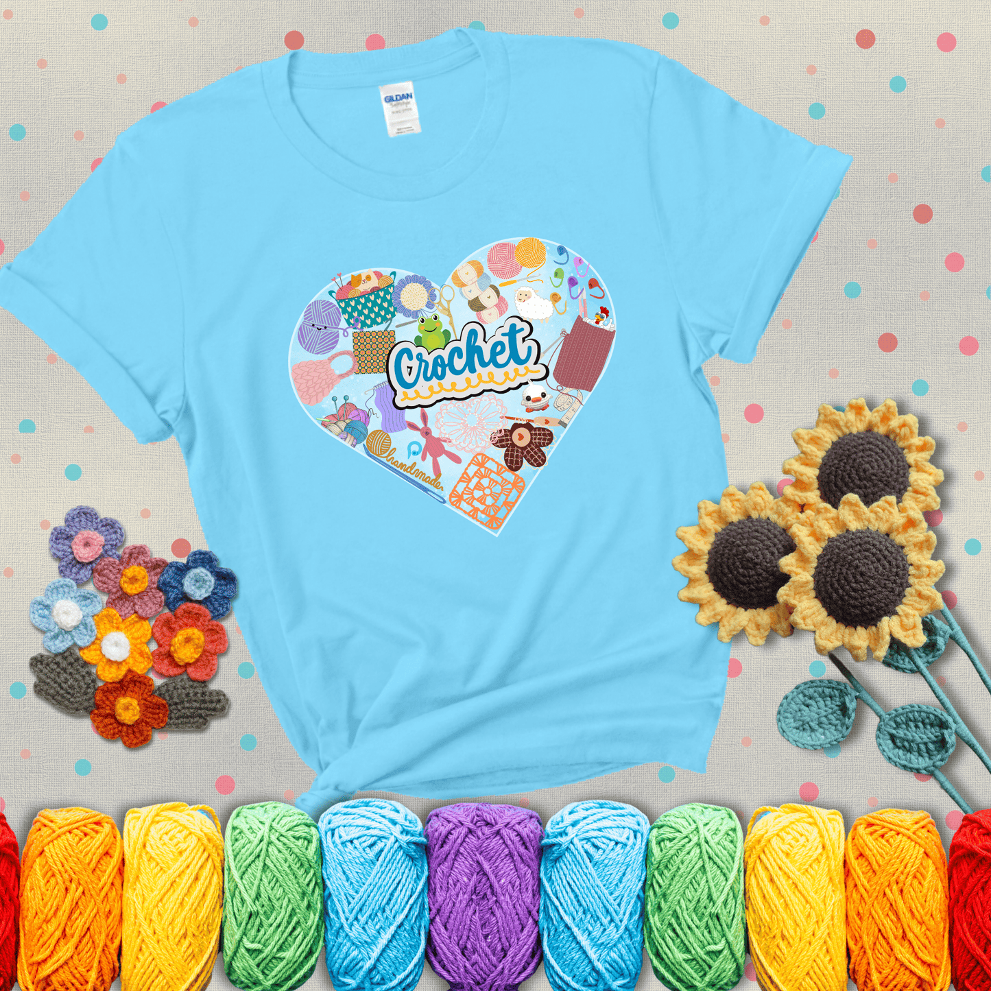 A heart filled with colorful crochet essentials including yarn, hooks, scissors, notions, and handmade items, with the word "Crochet" prominently in the center, showing a light blue tee with grey sunflower background