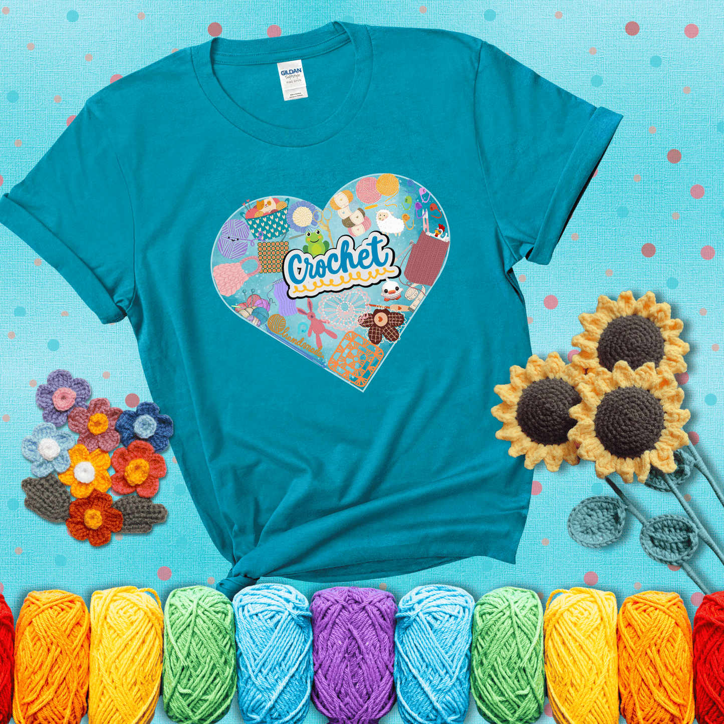 A heart filled with colorful crochet essentials including yarn, hooks, scissors, notions, and handmade items, with the word "Crochet" prominently in the center, showing a blue-green tee with a teal sunflower background