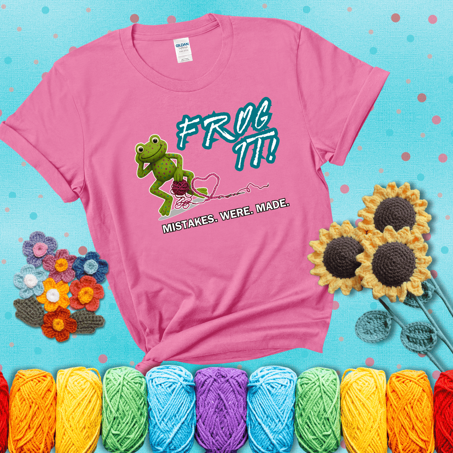 Green frog with yarn and heart-shaped loop. Text reads: “Frog It! Mistakes Were Made.” A playful crochet tee for anyone who's ever had to rip it back, showing a pink tee with a teal sunflower background