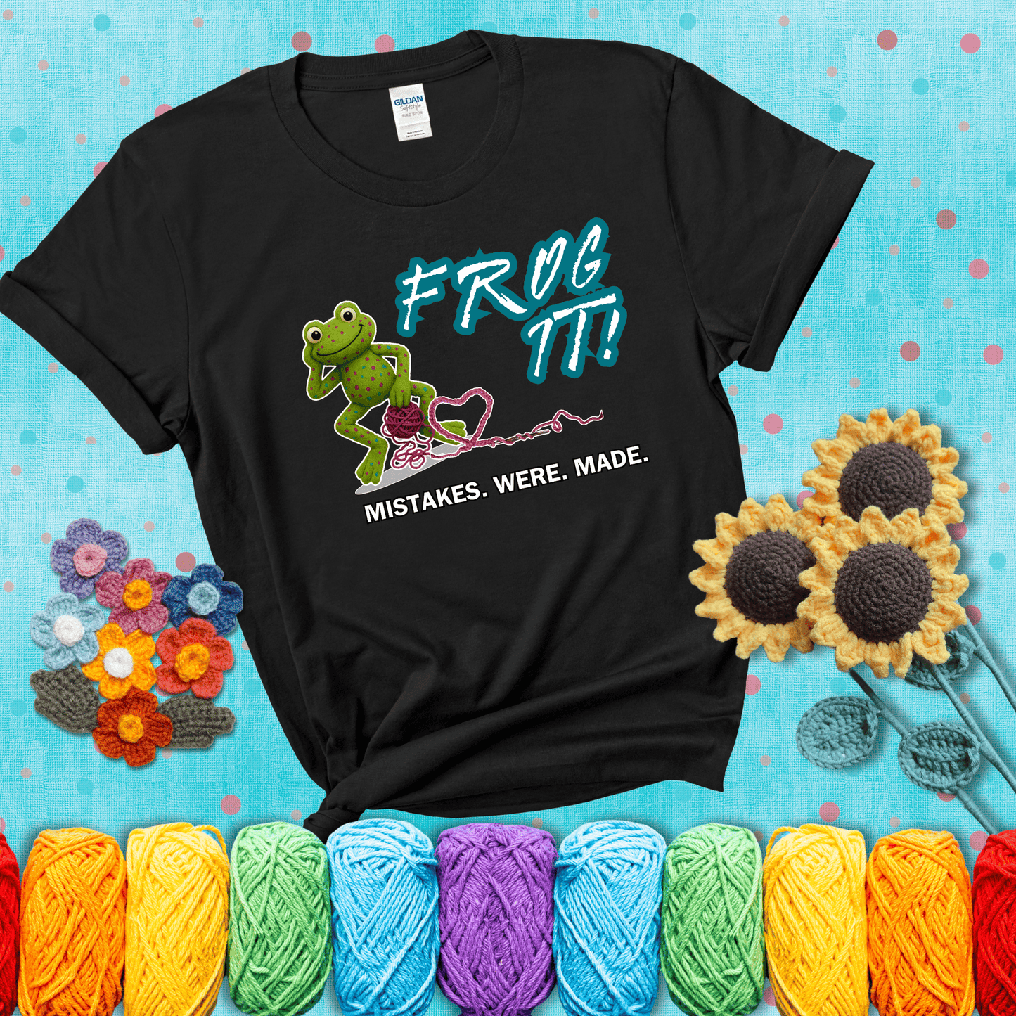 Green frog with yarn and heart-shaped loop. Text reads: “Frog It! Mistakes Were Made.” A playful crochet tee for anyone who's ever had to rip it back, showing a black tee with a teal sunflower background