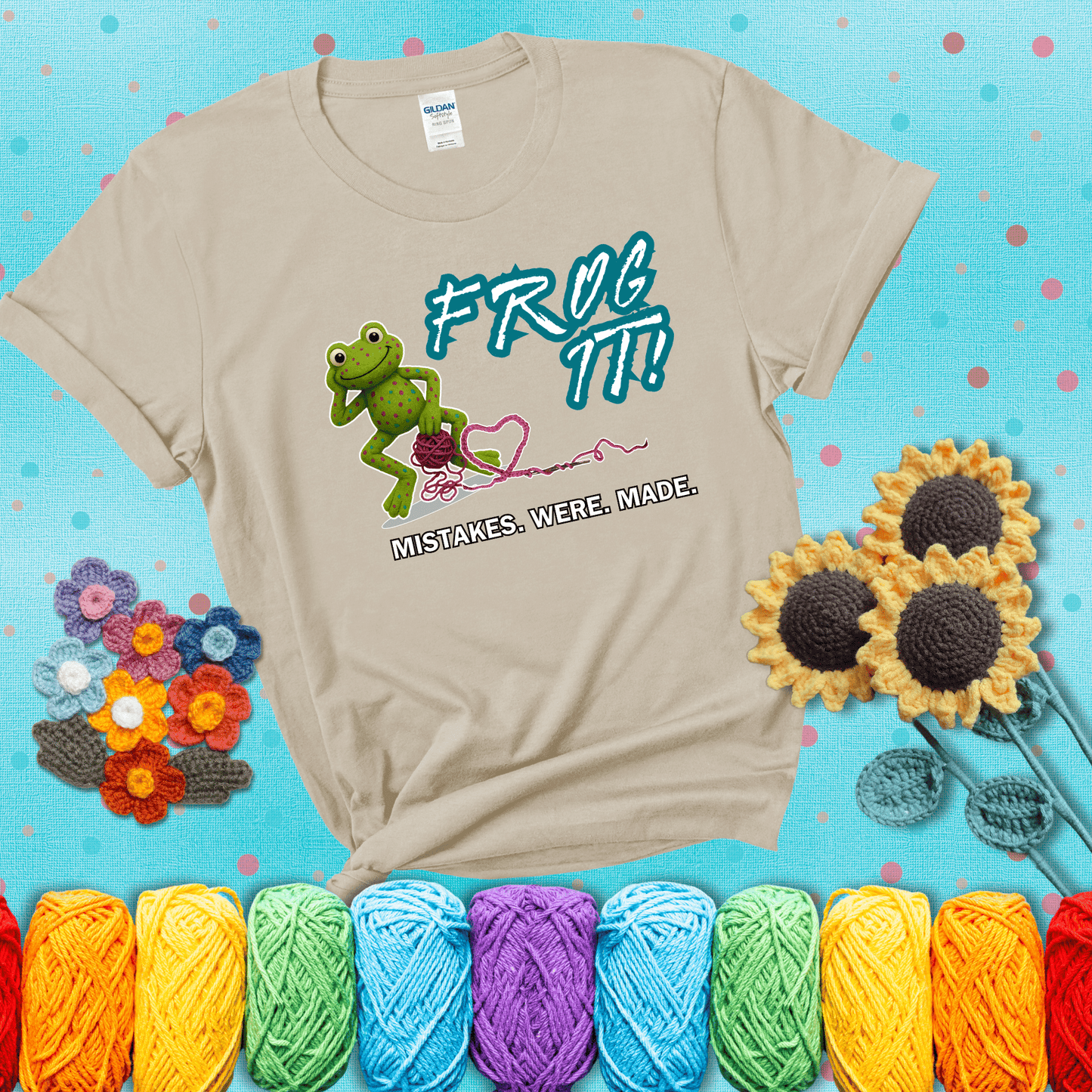 Green frog with yarn and heart-shaped loop. Text reads: “Frog It! Mistakes Were Made.” A playful crochet tee for anyone who's ever had to rip it back, showing a beige tee with a teal sunflower background