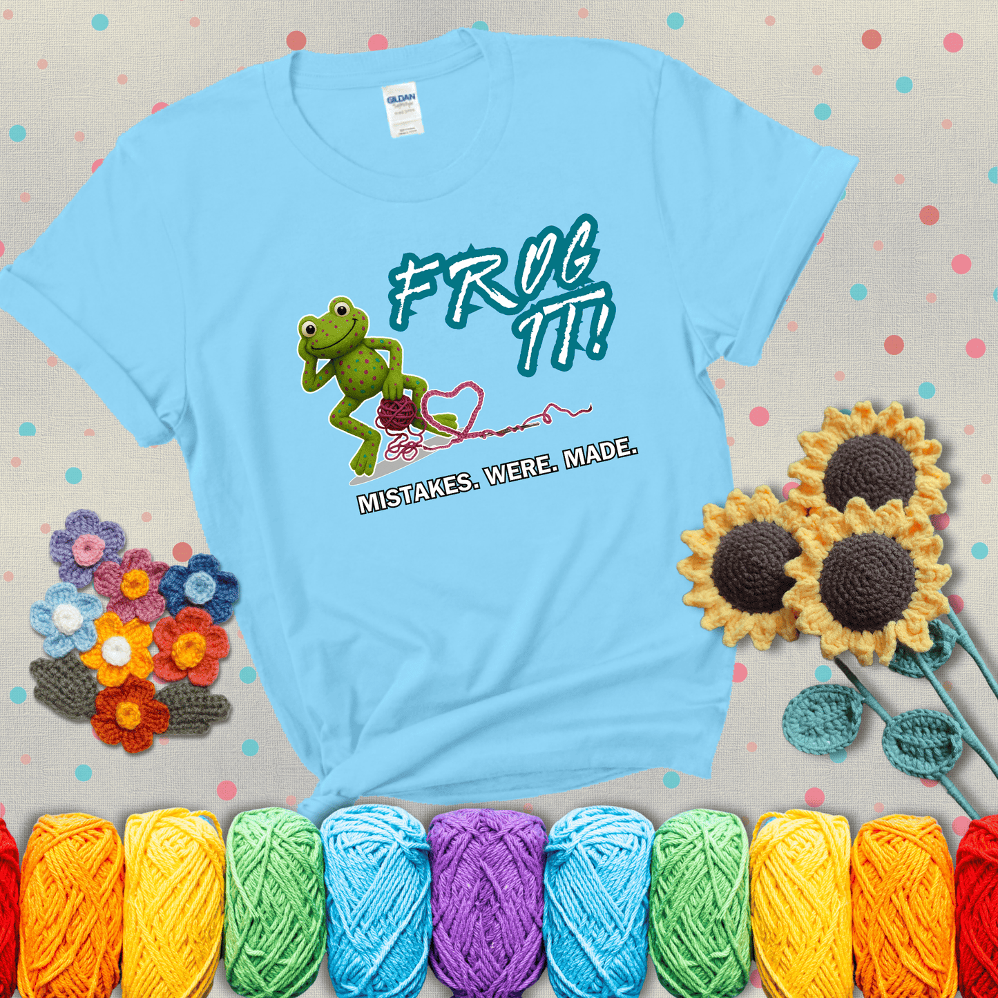 Green frog with yarn and heart-shaped loop. Text reads: “Frog It! Mistakes Were Made.” A playful crochet tee for anyone who's ever had to rip it back, showing a light blue tee with grey sunflower background
