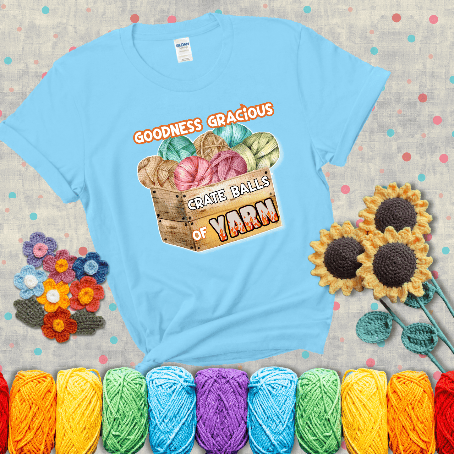 Wooden crate filled with colorful yarn balls and bold text “Goodness Gracious, Crate Balls of Yarn” with flame effects, a funny gift for crocheters showing a light blue tee with grey sunflower background