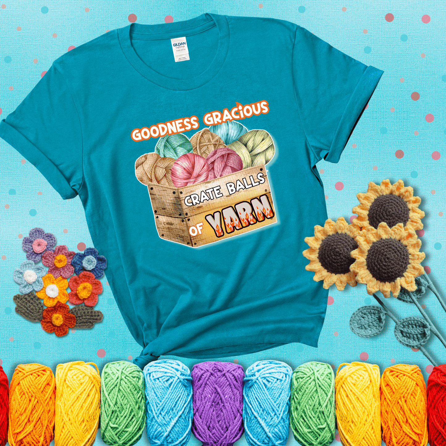 Wooden crate filled with colorful yarn balls and bold text “Goodness Gracious, Crate Balls of Yarn” with flame effects, a funny gift for crocheters showing a blue-green tee with a teal sunflower background