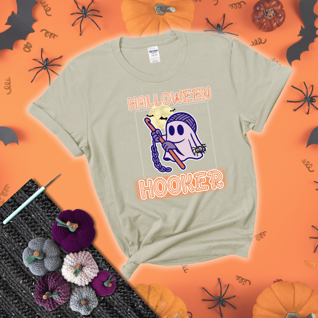 Cartoon ghost crocheter with a yarn ball head, crochet hook, bats, and text “Halloween Hooker,” a fun spooky tee for yarn lovers showing a beige tee with a festive Halloween background