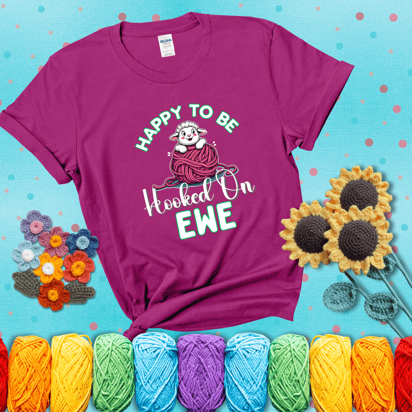 Smiling cartoon sheep peeks from a pink yarn ball, surrounded by green text “Happy to Be Hooked on Ewe” — playful and affectionate sheep pun for crocheters showing a magenta tee with a teal sunflower background