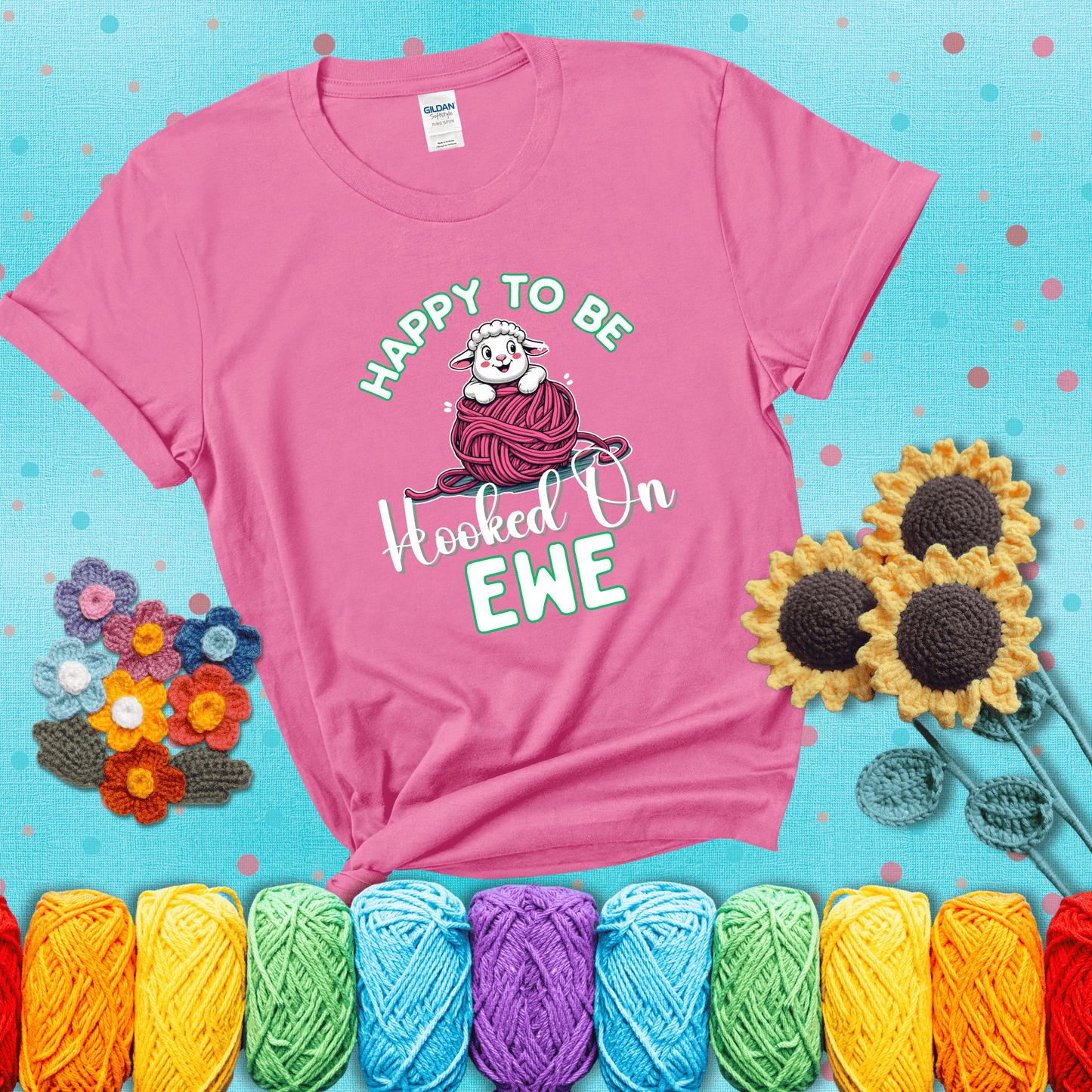 Smiling cartoon sheep peeks from a pink yarn ball, surrounded by green text “Happy to Be Hooked on Ewe” — playful and affectionate sheep pun for crocheters showing a pink tee with a teal sunflower background