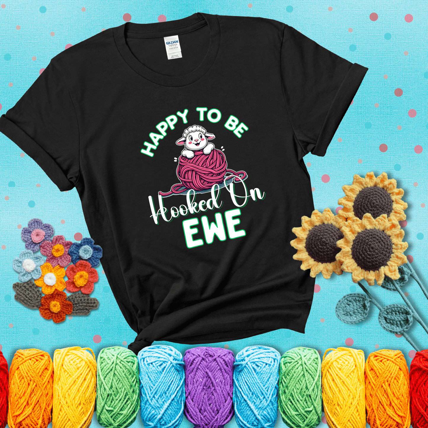 Smiling cartoon sheep peeks from a pink yarn ball, surrounded by green text “Happy to Be Hooked on Ewe” — playful and affectionate sheep pun for crocheters showing a black tee with a teal sunflower background