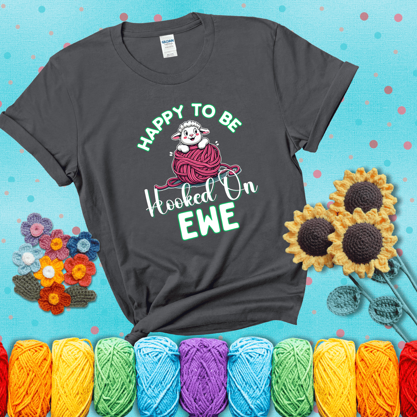 Smiling cartoon sheep peeks from a pink yarn ball, surrounded by green text “Happy to Be Hooked on Ewe” — playful and affectionate sheep pun for crocheters showing a dark grey tee with a teal sunflower background