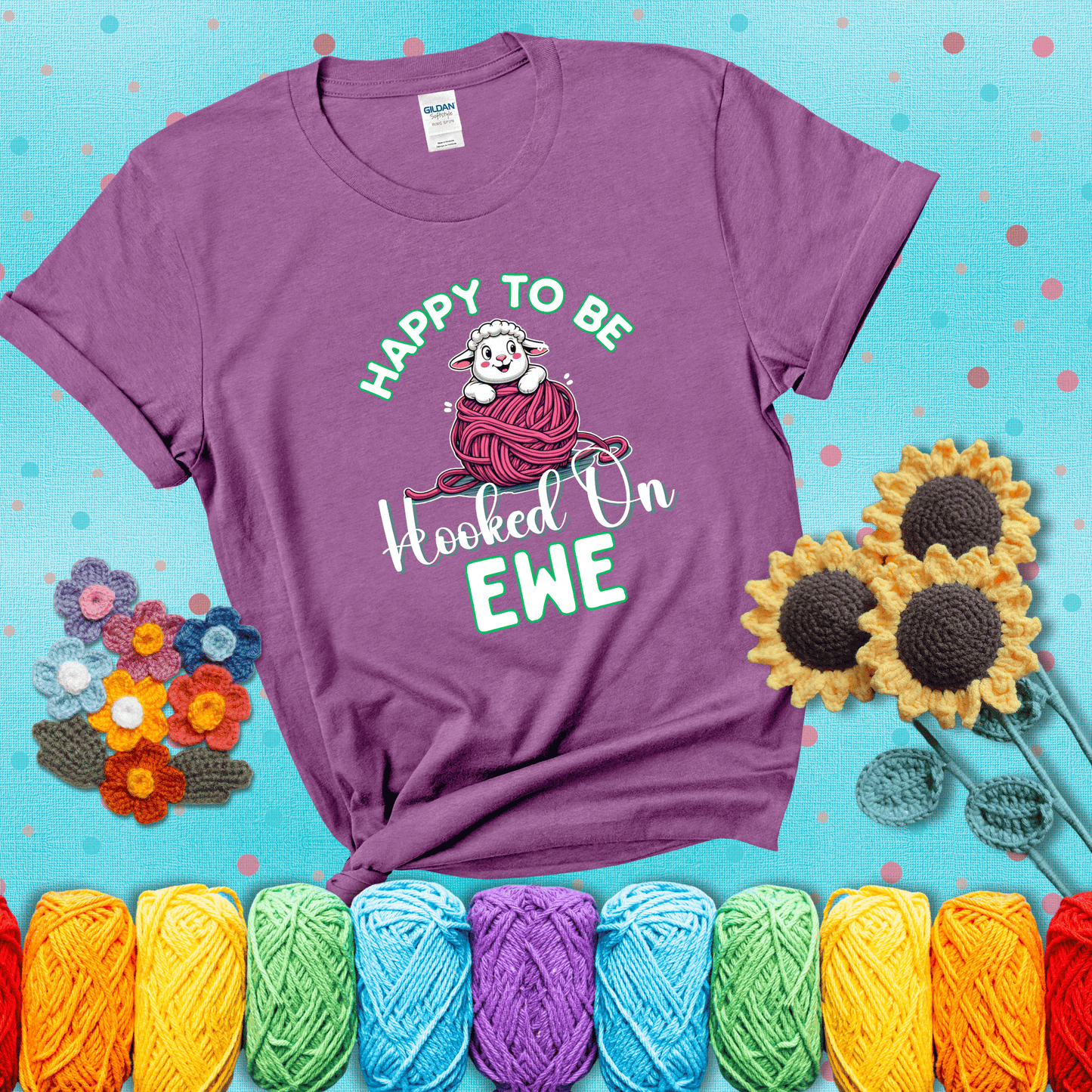 Smiling cartoon sheep peeks from a pink yarn ball, surrounded by green text “Happy to Be Hooked on Ewe” — playful and affectionate sheep pun for crocheters showing a light purple tee with a teal sunflower background