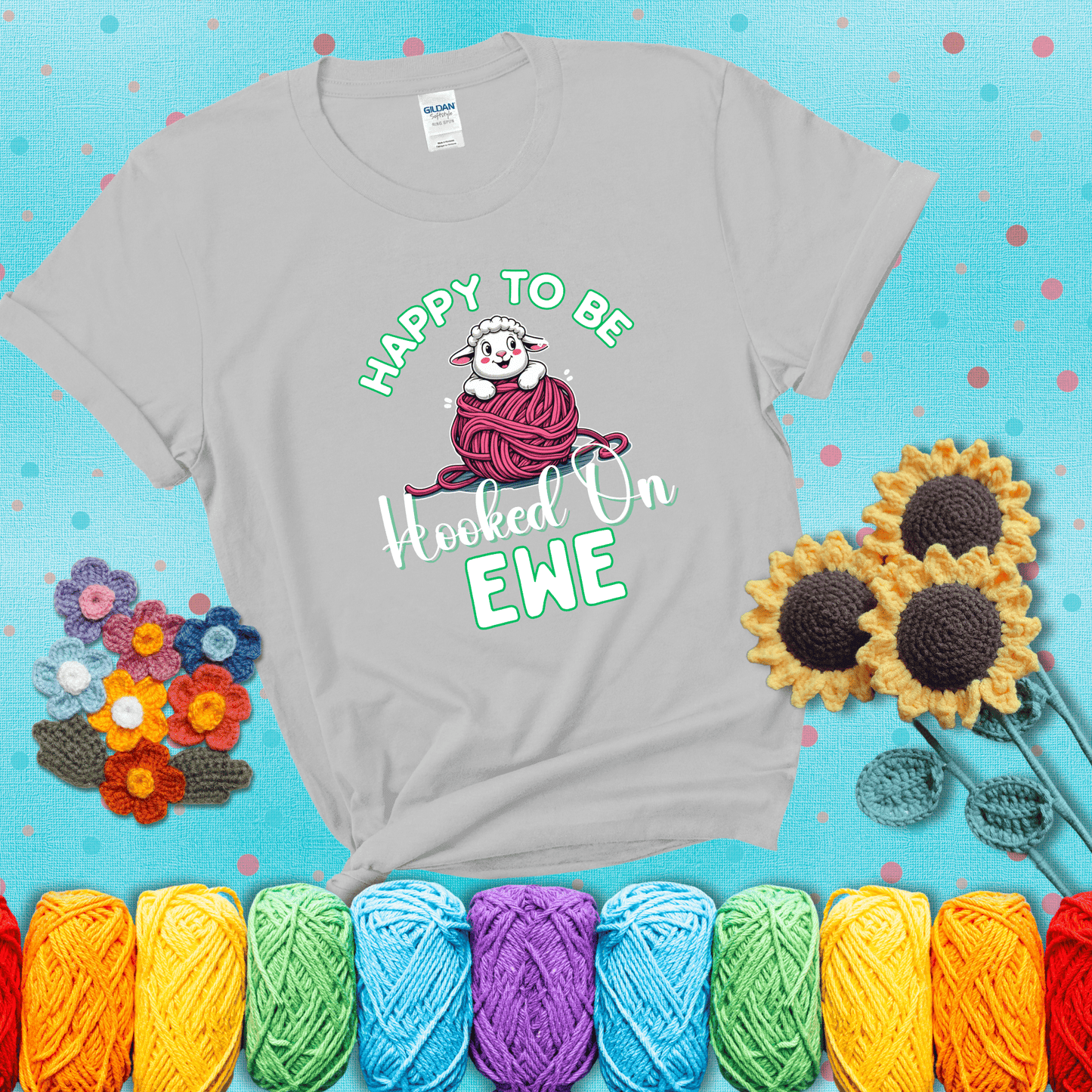 Smiling cartoon sheep peeks from a pink yarn ball, surrounded by green text “Happy to Be Hooked on Ewe” — playful and affectionate sheep pun for crocheters showing a light grey tee with a teal sunflower background
