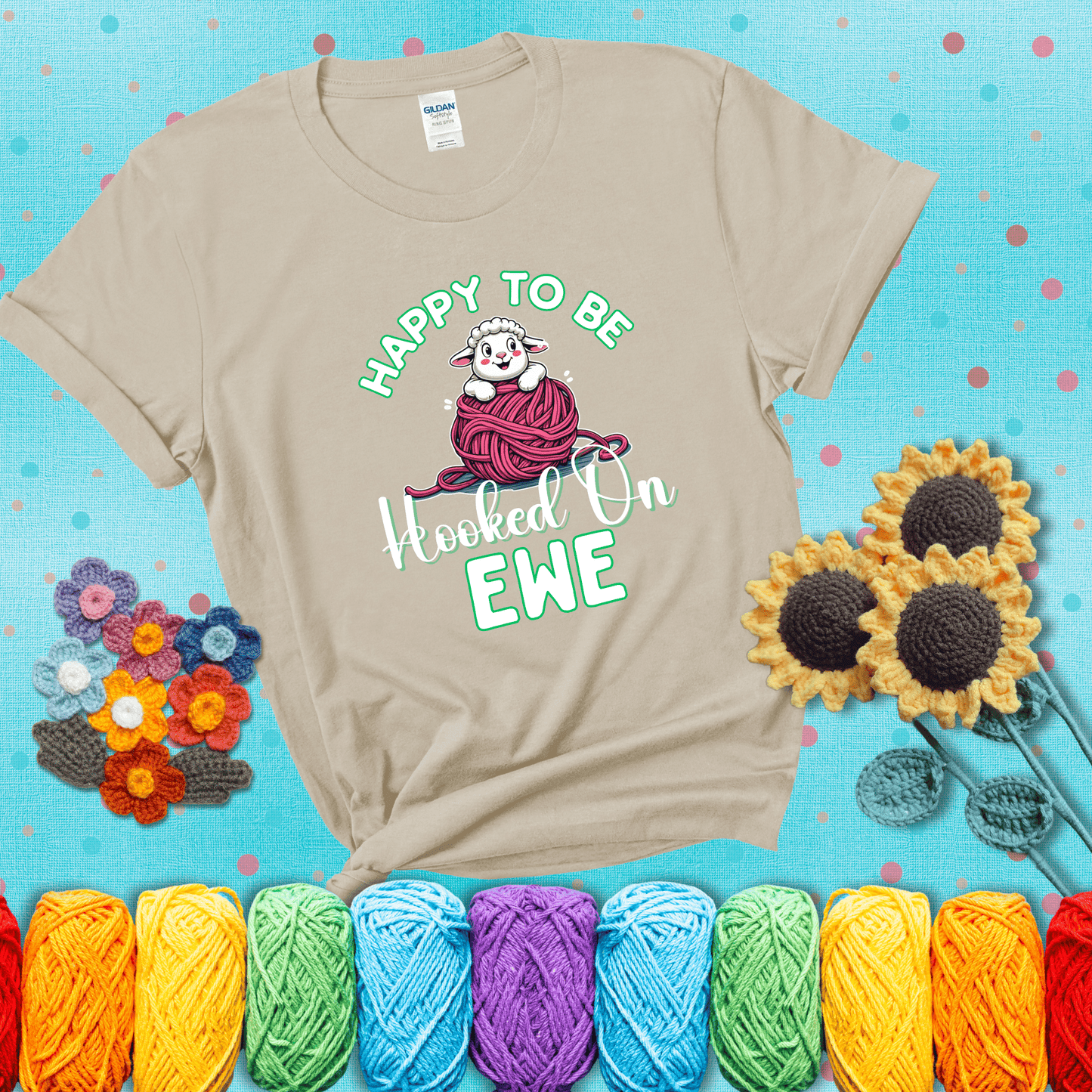 Smiling cartoon sheep peeks from a pink yarn ball, surrounded by green text “Happy to Be Hooked on Ewe” — playful and affectionate sheep pun for crocheters showing a beige tee with a teal sunflower background