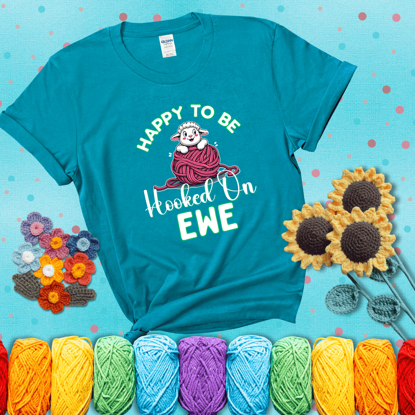 Smiling cartoon sheep peeks from a pink yarn ball, surrounded by green text “Happy to Be Hooked on Ewe” — playful and affectionate sheep pun for crocheters showing a blue-green tee with a teal sunflower background