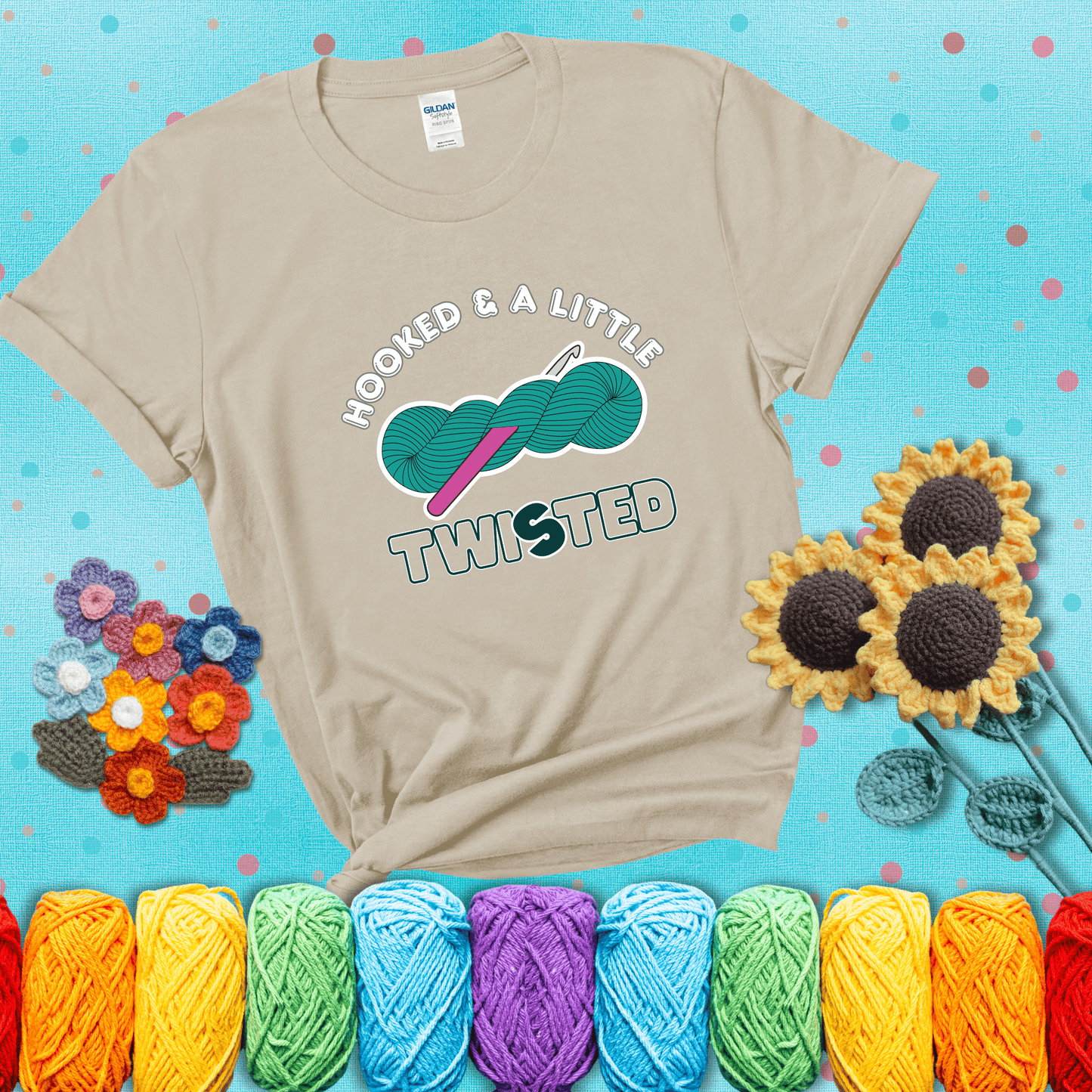 A teal skein of yarn with a hot pink crochet hook through it, captioned “Hooked & a Little Twisted” showing a beige tee with a teal sunflower background