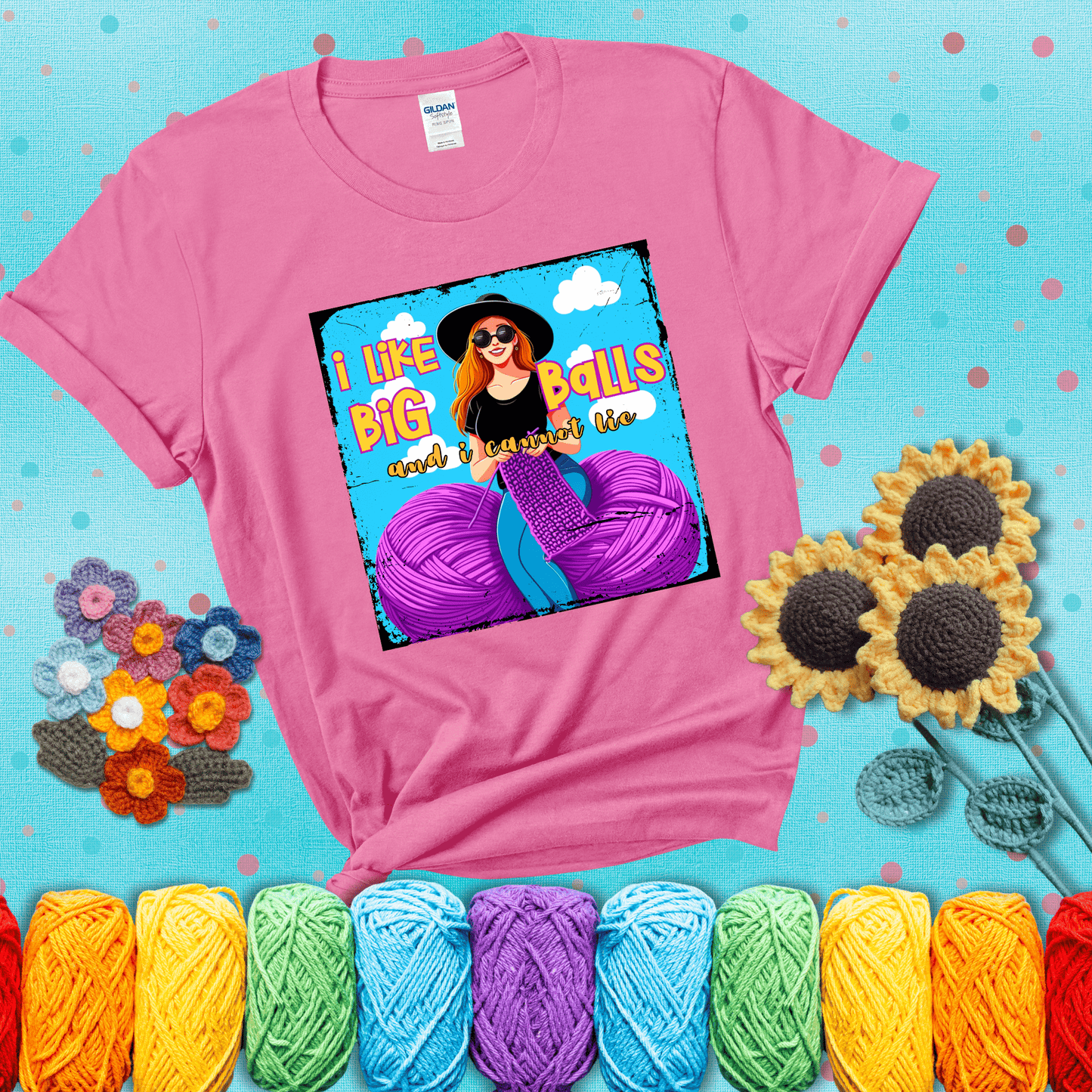 Bold cartoon image of a woman crocheting between two giant purple yarn balls with the phrase “I like big balls and I cannot lie” in retro fonts showing a pink tee with a teal sunflower background