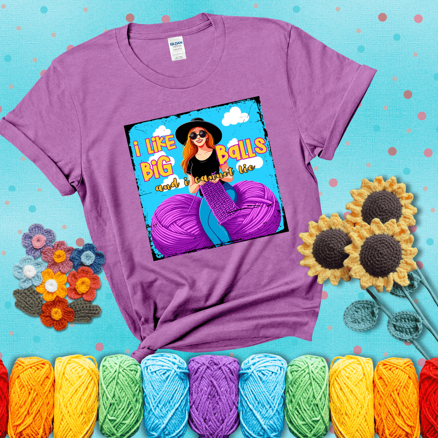 Bold cartoon image of a woman crocheting between two giant purple yarn balls with the phrase “I like big balls and I cannot lie” in retro fonts showing a light purple tee with a teal sunflower background