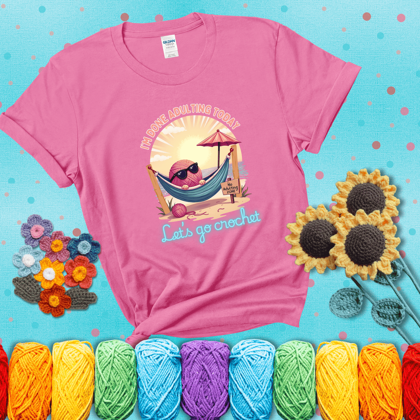 A chill yarn ball wearing sunglasses lounges in a hammock on a beach under the sun with the phrase “I’m done adulting today – Let’s go crochet,” showing a pink tee with a teal sunflower background