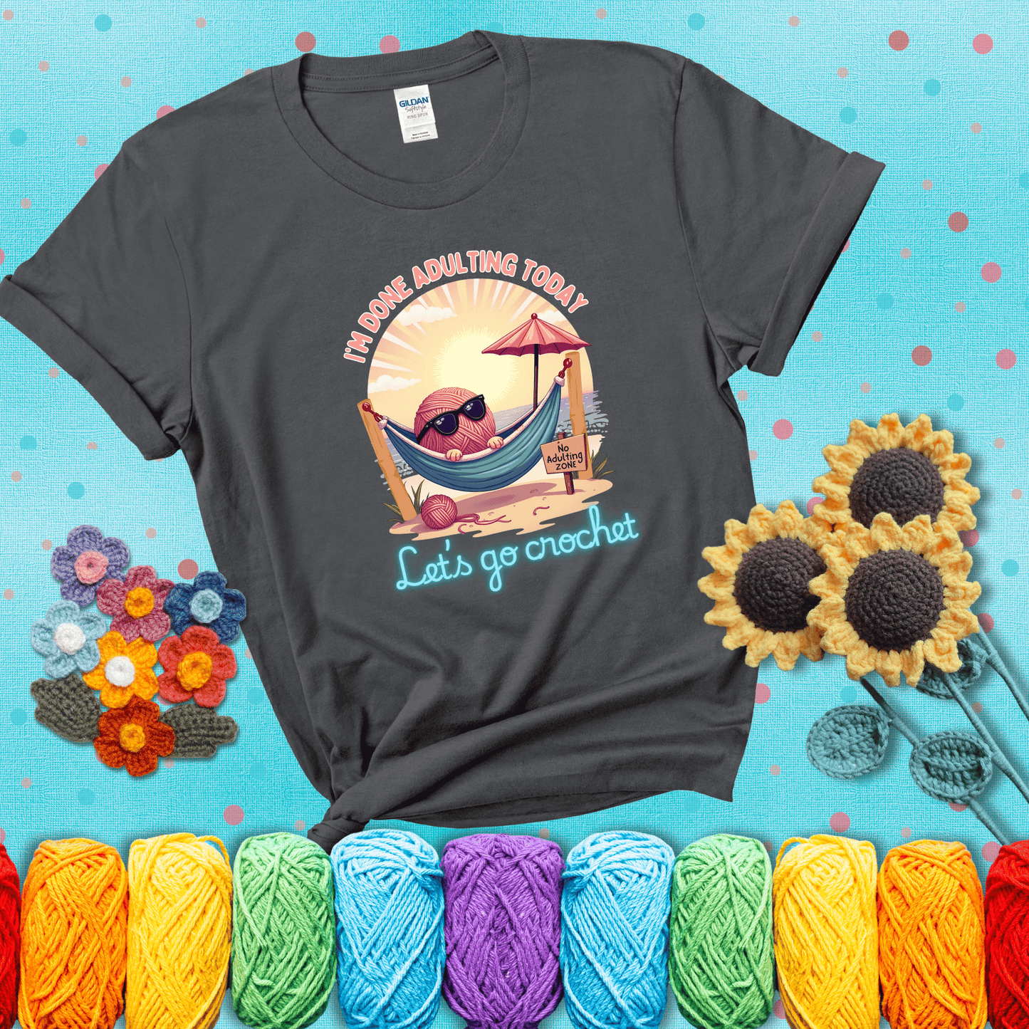 A chill yarn ball wearing sunglasses lounges in a hammock on a beach under the sun with the phrase “I’m done adulting today – Let’s go crochet,” showing a dark grey tee with a teal sunflower background