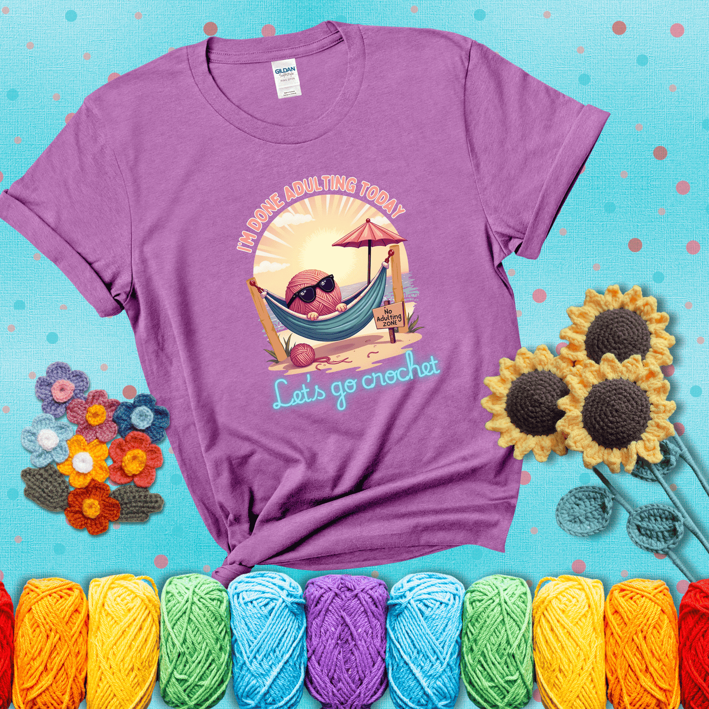 A chill yarn ball wearing sunglasses lounges in a hammock on a beach under the sun with the phrase “I’m done adulting today – Let’s go crochet,” showing a light purple tee with a teal sunflower background