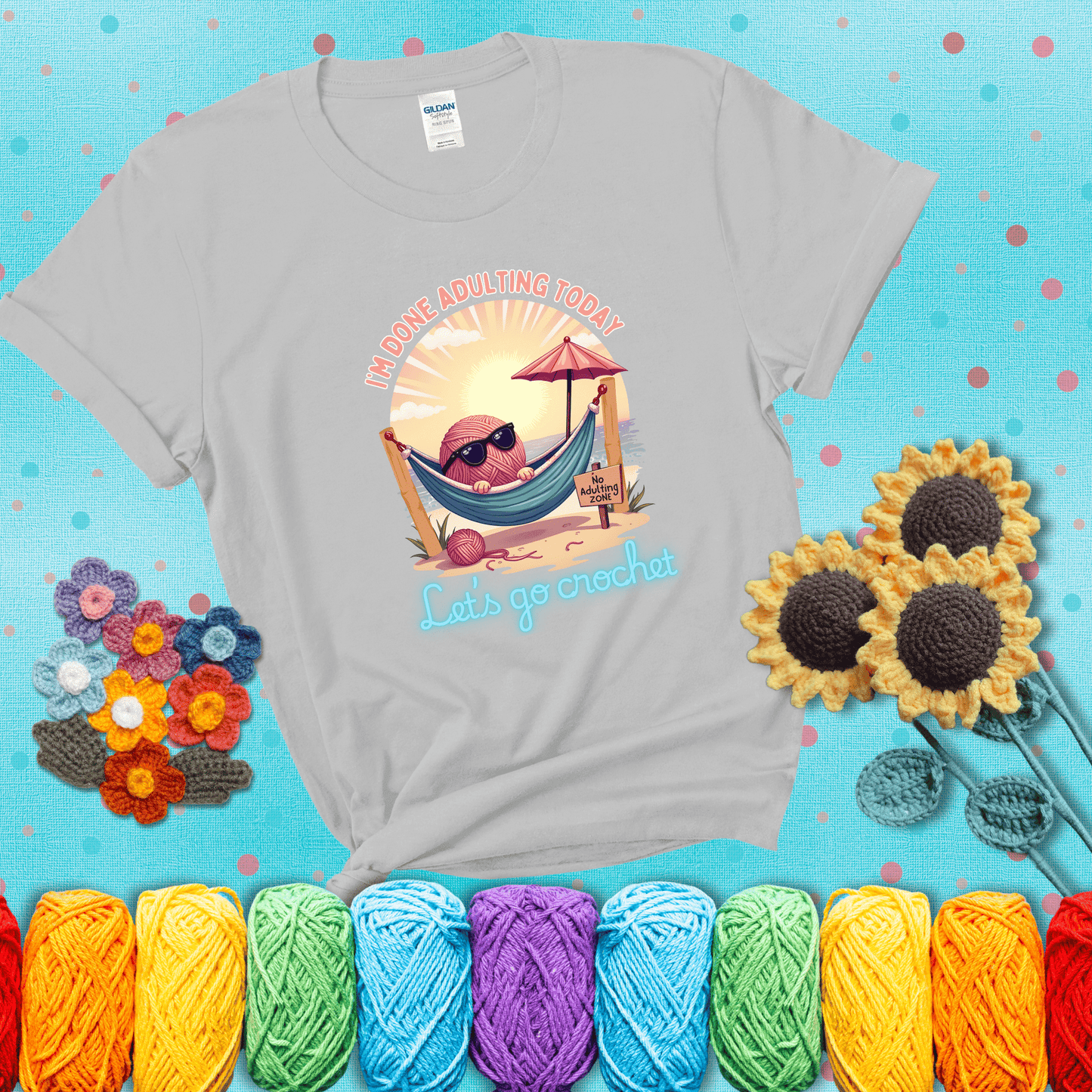 A chill yarn ball wearing sunglasses lounges in a hammock on a beach under the sun with the phrase “I’m done adulting today – Let’s go crochet,” showing a light grey tee with a teal sunflower background