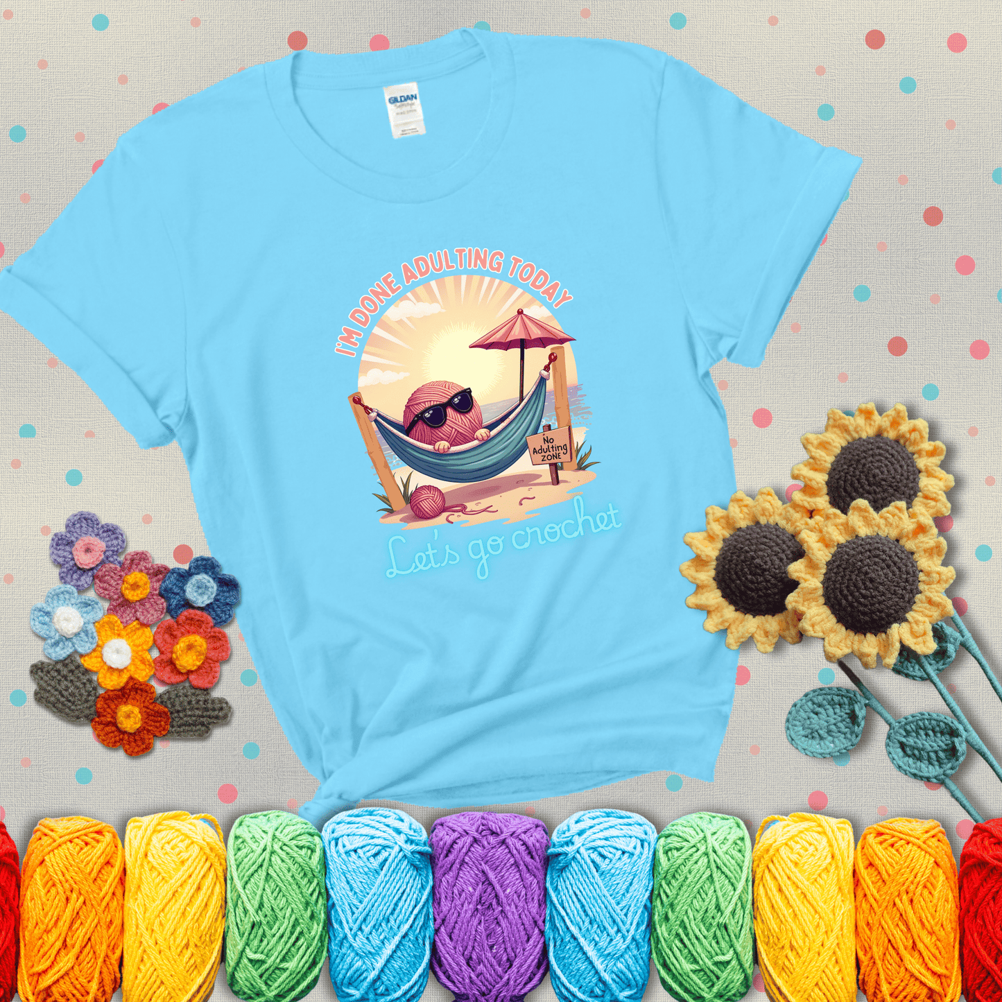 A chill yarn ball wearing sunglasses lounges in a hammock on a beach under the sun with the phrase “I’m done adulting today – Let’s go crochet,” showing a light blue tee with grey sunflower background