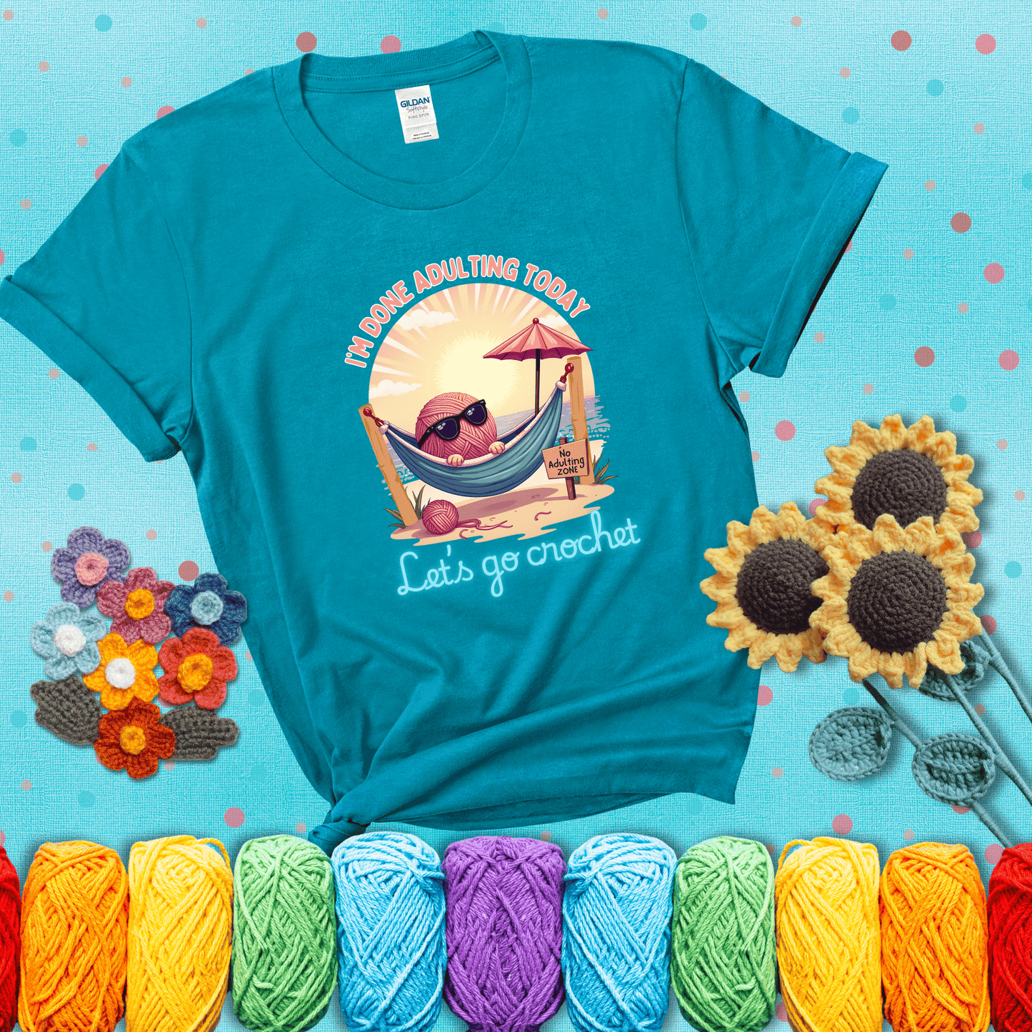 A chill yarn ball wearing sunglasses lounges in a hammock on a beach under the sun with the phrase “I’m done adulting today – Let’s go crochet,” showing a blue-green tee with a teal sunflower background