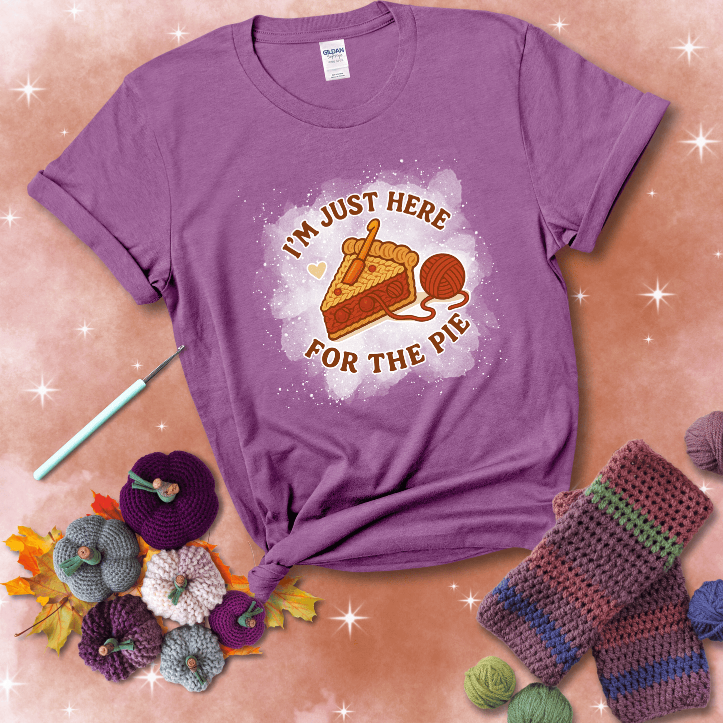 A slice of cherry pie with a crochet hook tucked in the filling and yarn trailing out, blending baking with crochet fun, showing a light purple tee with a festive Fall background