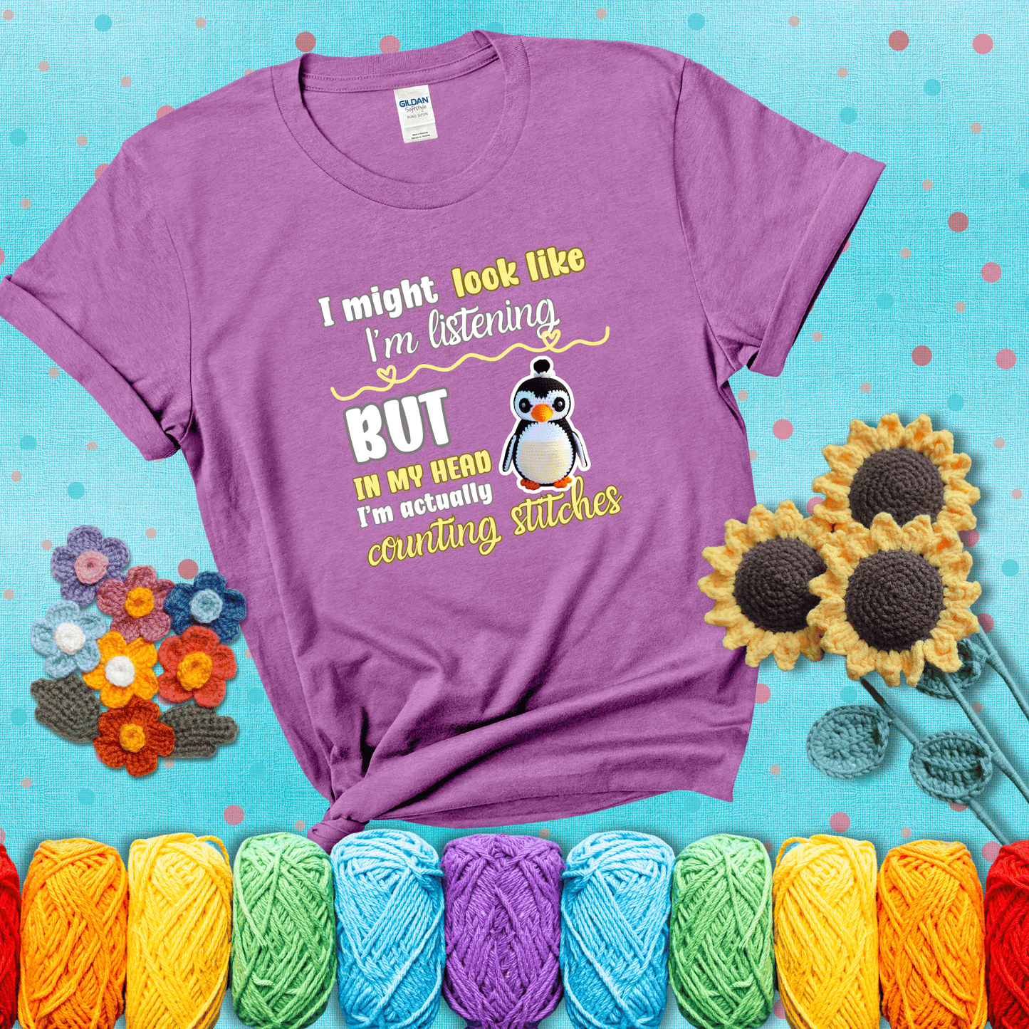 Crochet penguin next to the text “I might look like I’m listening but in my head I’m actually counting stitches” showing a light purple tee with a teal sunflower background