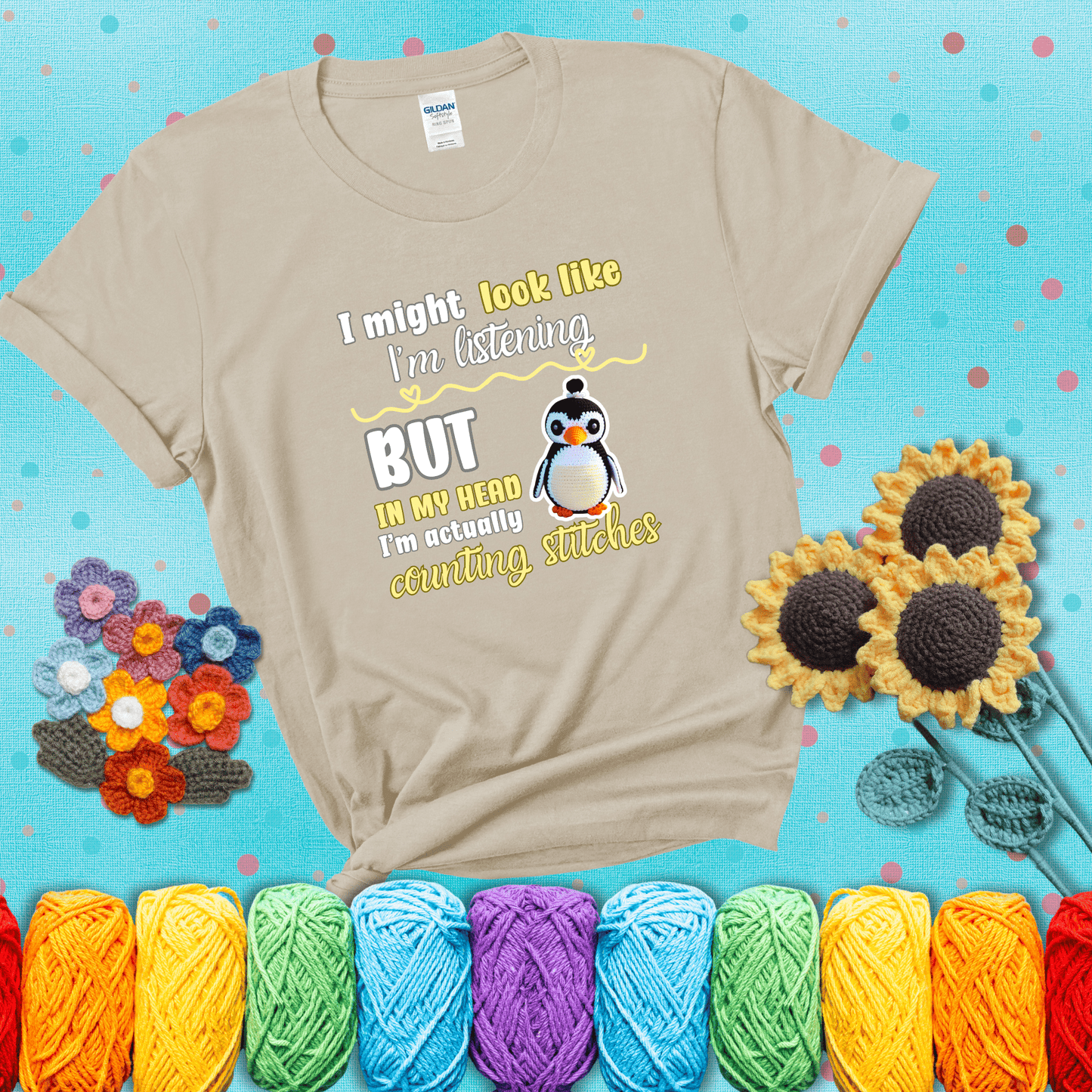 Crochet penguin next to the text “I might look like I’m listening but in my head I’m actually counting stitches” showing a beige tee with a teal sunflower background