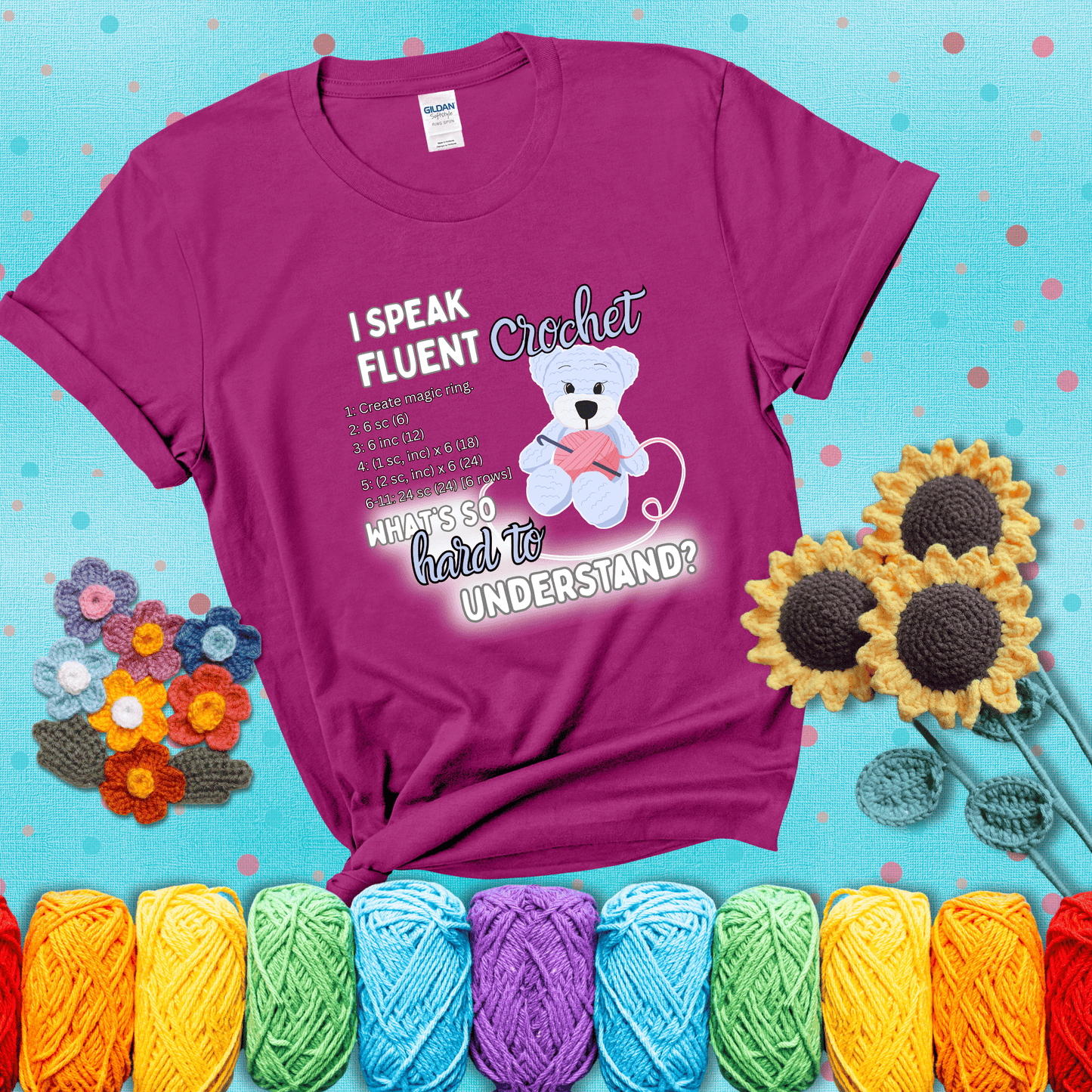 A cute crochet bear holding a yarn ball, surrounded by a short crochet pattern. The phrase reads “I Speak Fluent Crochet – What’s so hard to understand?” showing a magenta tee with a teal sunflower background