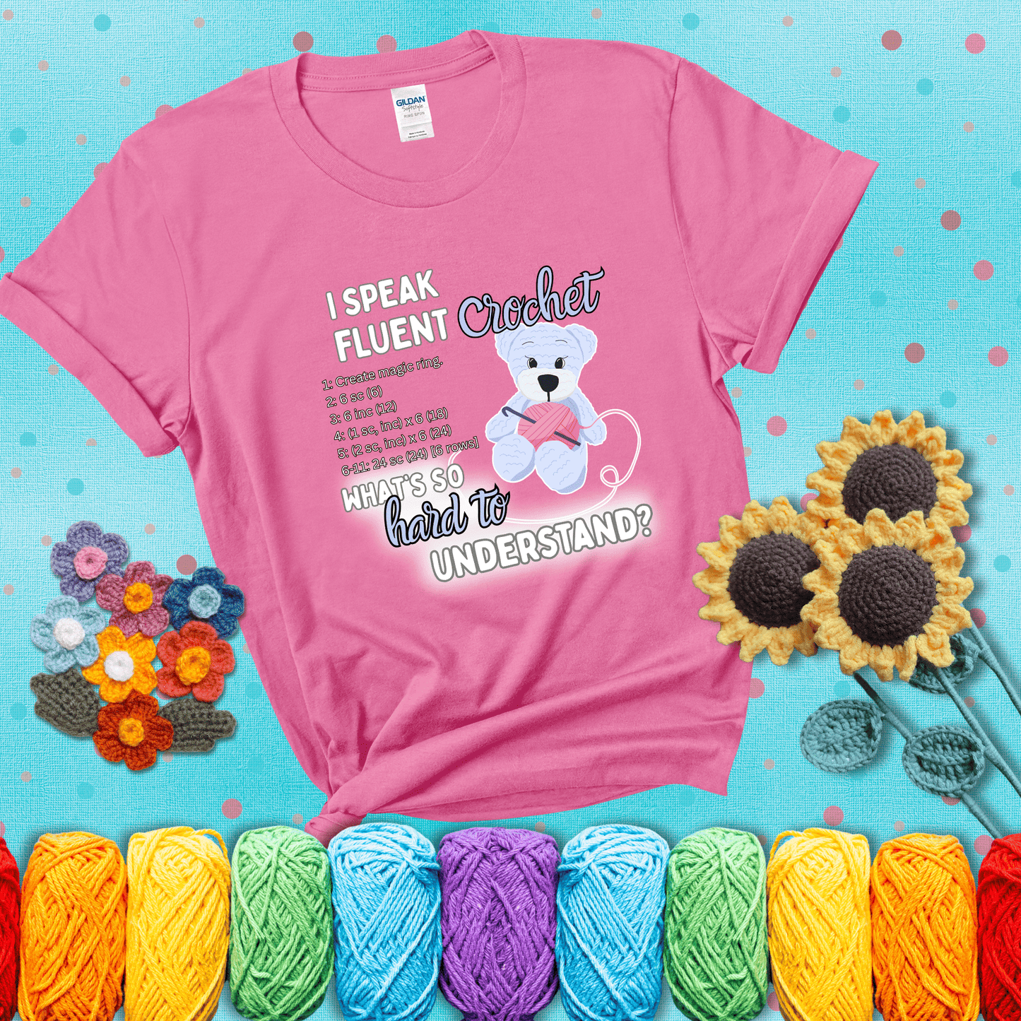 A cute crochet bear holding a yarn ball, surrounded by a short crochet pattern. The phrase reads “I Speak Fluent Crochet – What’s so hard to understand?” showing a pink tee with a teal sunflower background