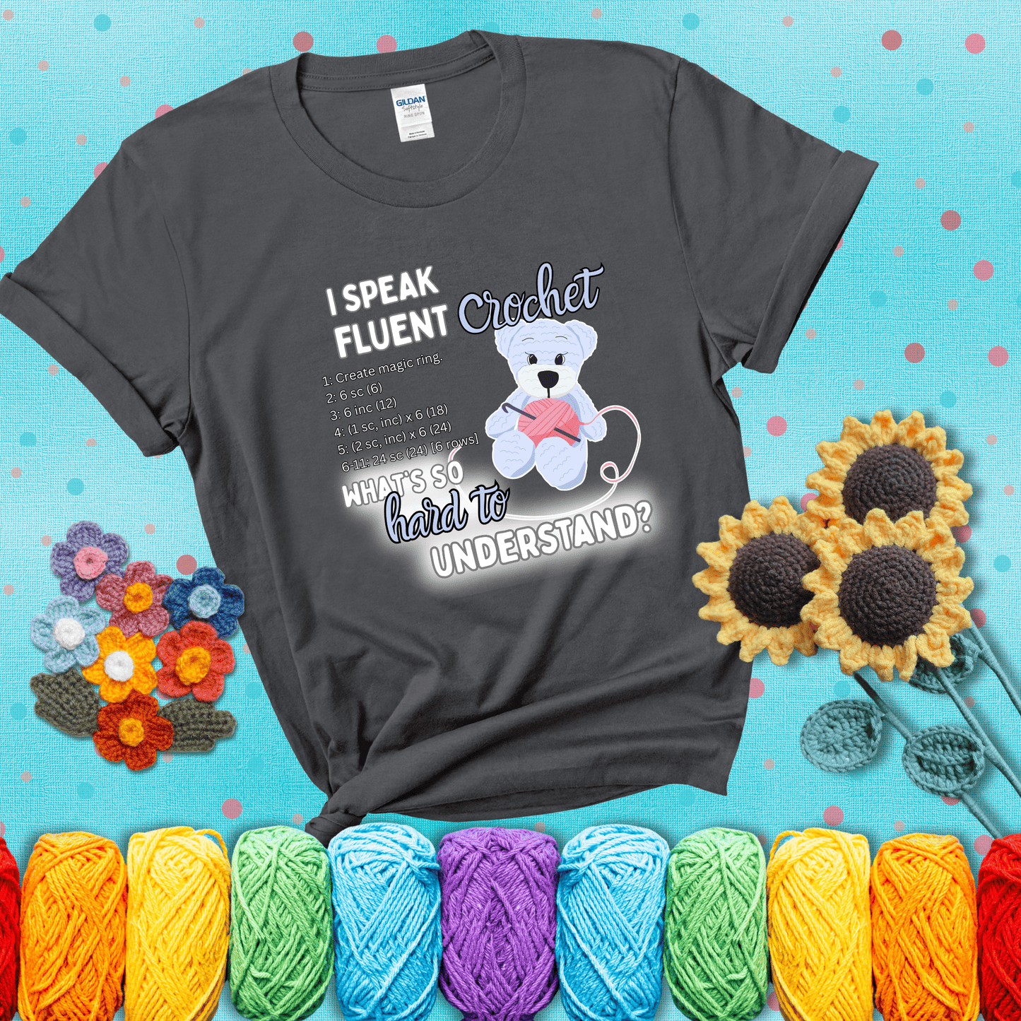 A cute crochet bear holding a yarn ball, surrounded by a short crochet pattern. The phrase reads “I Speak Fluent Crochet – What’s so hard to understand?” showing a dark grey tee with a teal sunflower background