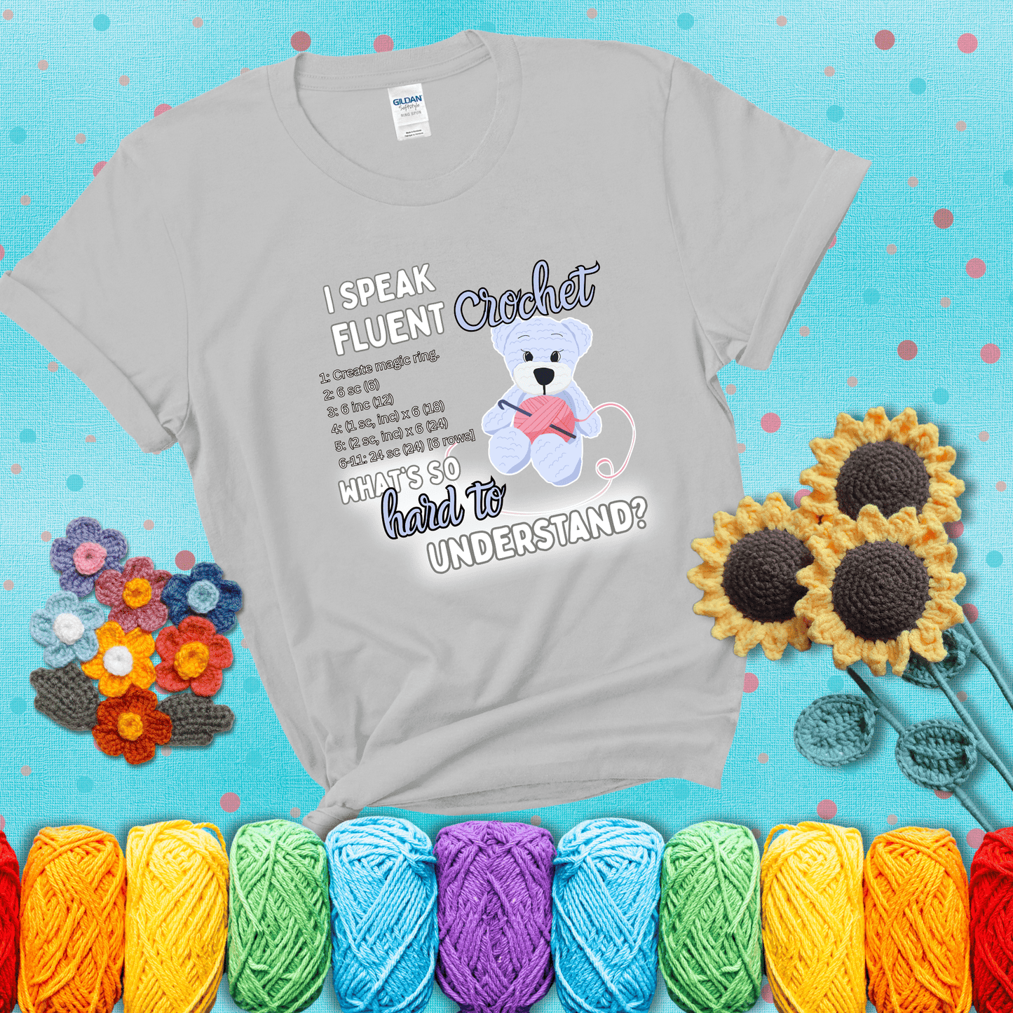 A cute crochet bear holding a yarn ball, surrounded by a short crochet pattern. The phrase reads “I Speak Fluent Crochet – What’s so hard to understand?” showing a light grey tee with a teal sunflower background