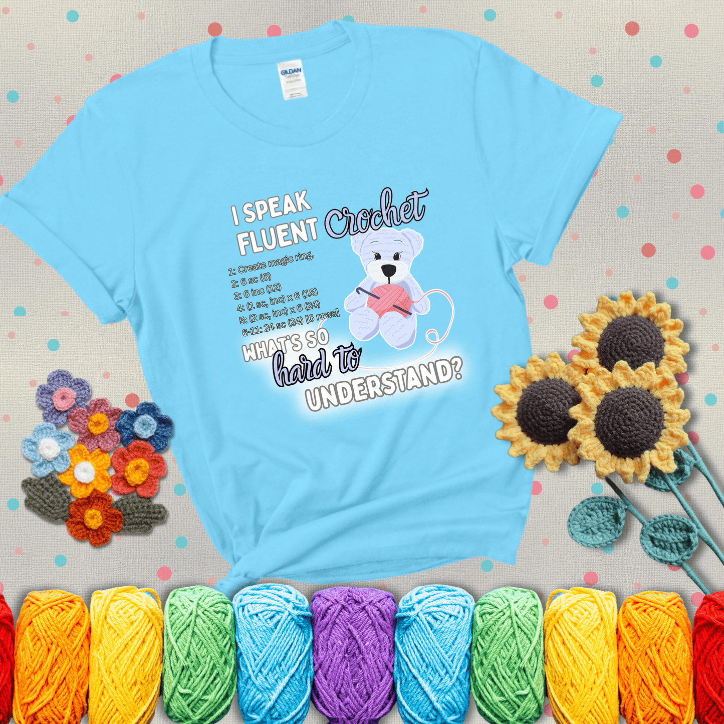 A cute crochet bear holding a yarn ball, surrounded by a short crochet pattern. The phrase reads “I Speak Fluent Crochet – What’s so hard to understand?” showing a light blue tee with grey sunflower background