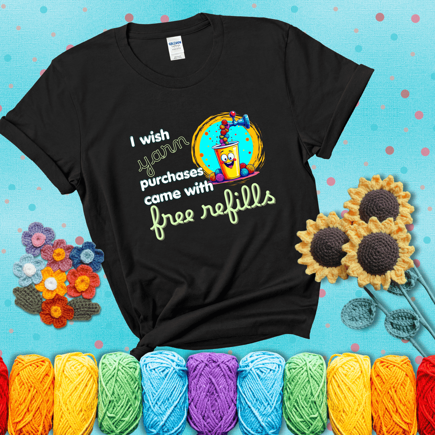 A bright yellow cup with a smiling face is being filled with colorful yarn balls from a soda machine, with the phrase “I wish yarn purchases came with free refills,” showing a black tee with a teal sunflower background