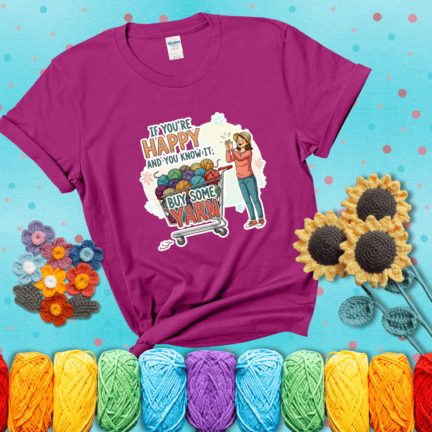 Woman clapping beside a shopping cart overflowing with colorful yarn balls, styled with cheerful pastel accents and bold playful lettering showing a magenta tee with a teal sunflower background