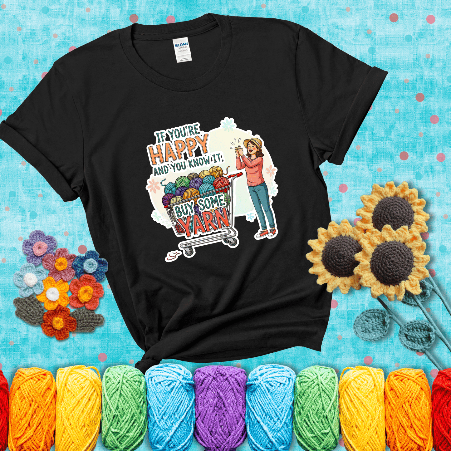 Woman clapping beside a shopping cart overflowing with colorful yarn balls, styled with cheerful pastel accents and bold playful lettering showing a black tee with a teal sunflower background