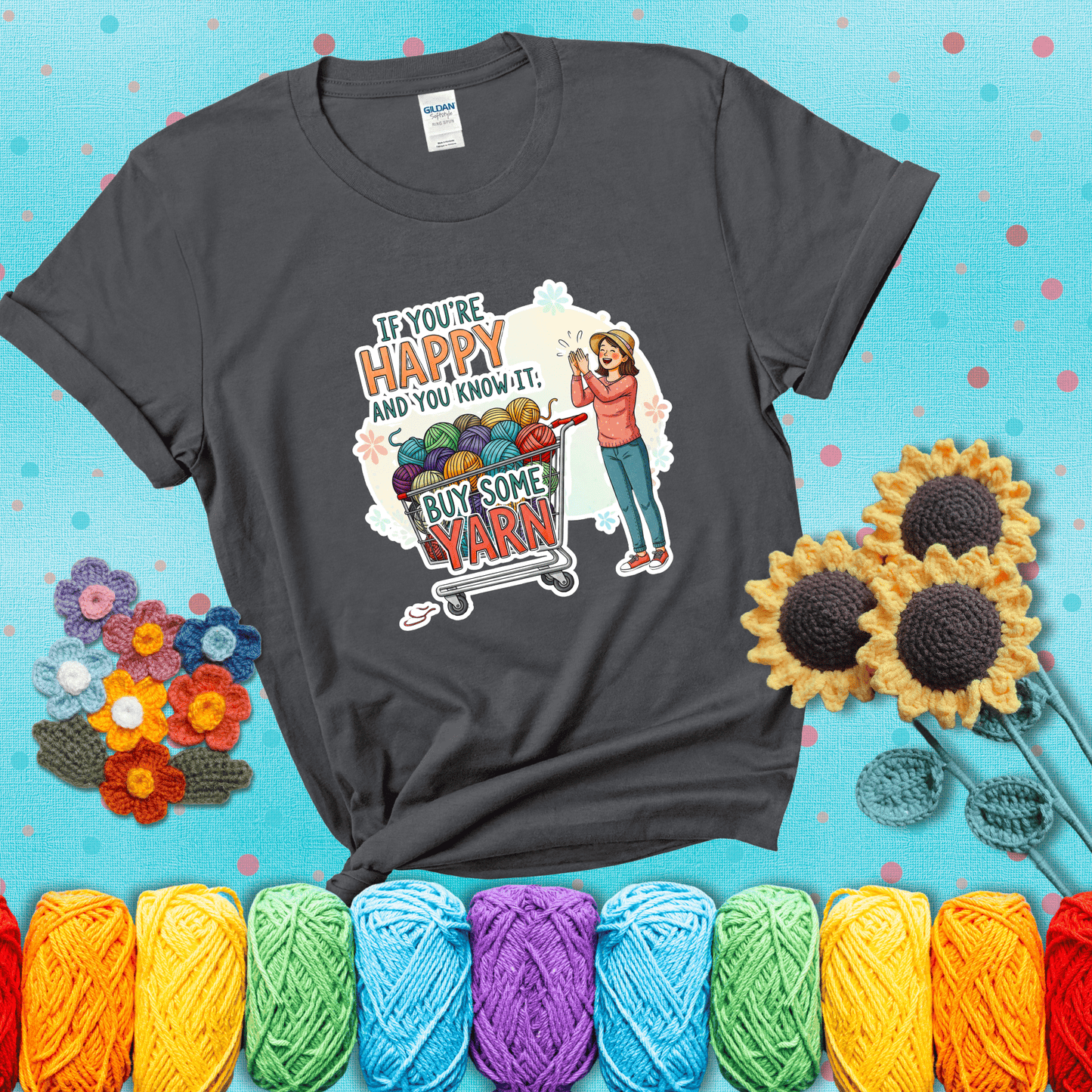 Woman clapping beside a shopping cart overflowing with colorful yarn balls, styled with cheerful pastel accents and bold playful lettering showing a dark grey tee with a teal sunflower background